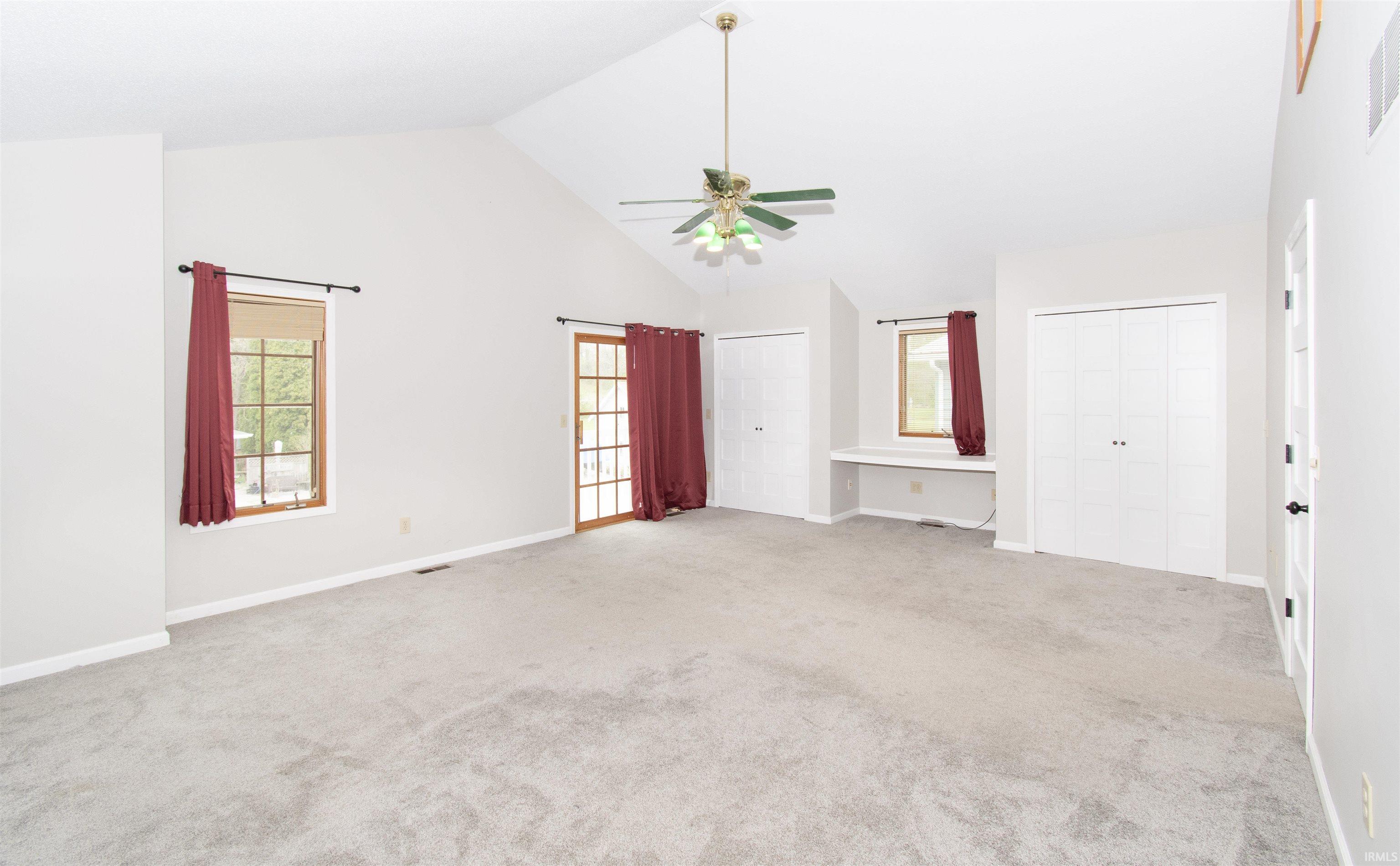 Spacious room featuring vaulted ceilings, light gray carpeting, and a central ceiling fan with integrated lighting