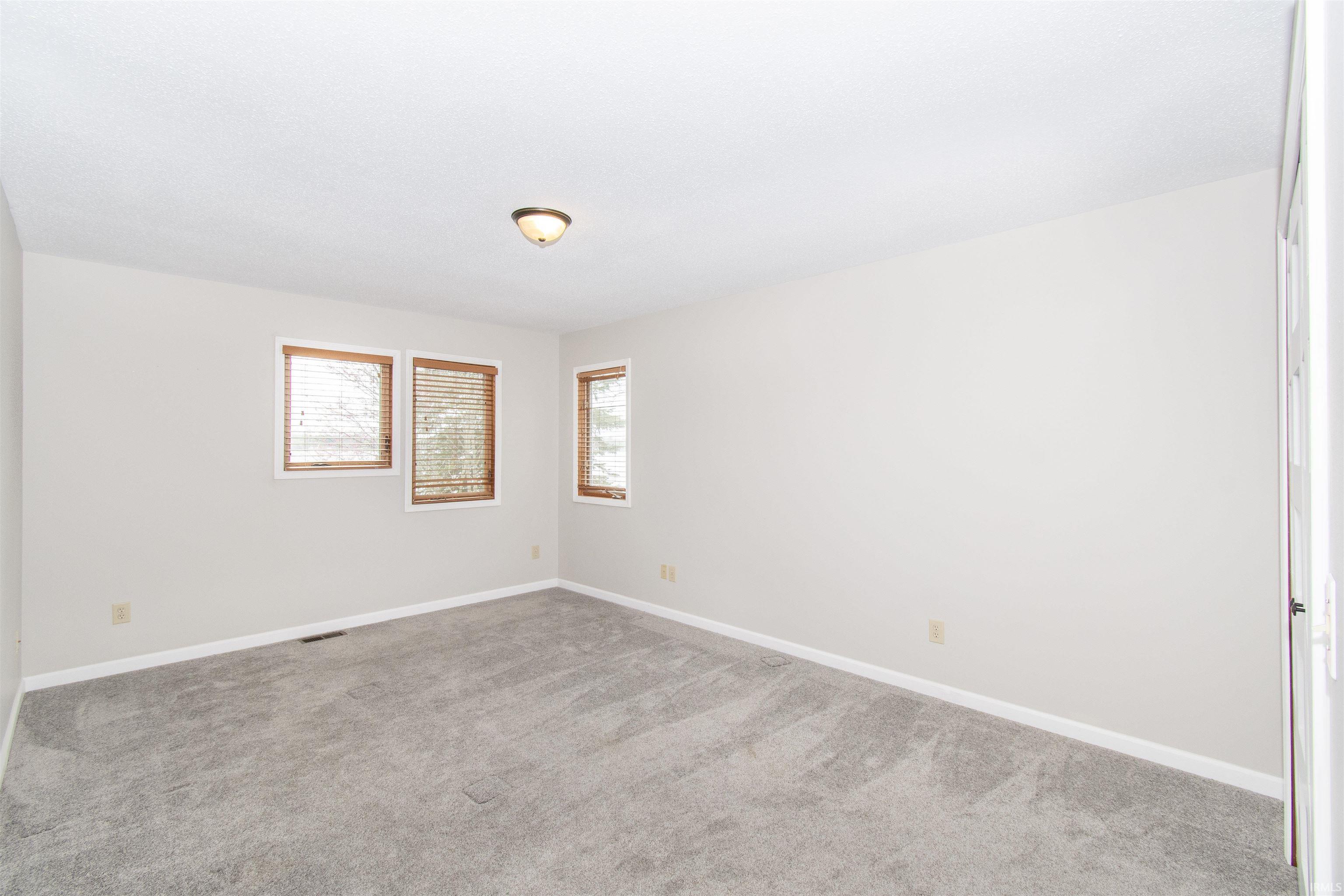 Spacious interior room with light gray carpeting, neutral wall finishes, and multiple windows featuring wood blinds