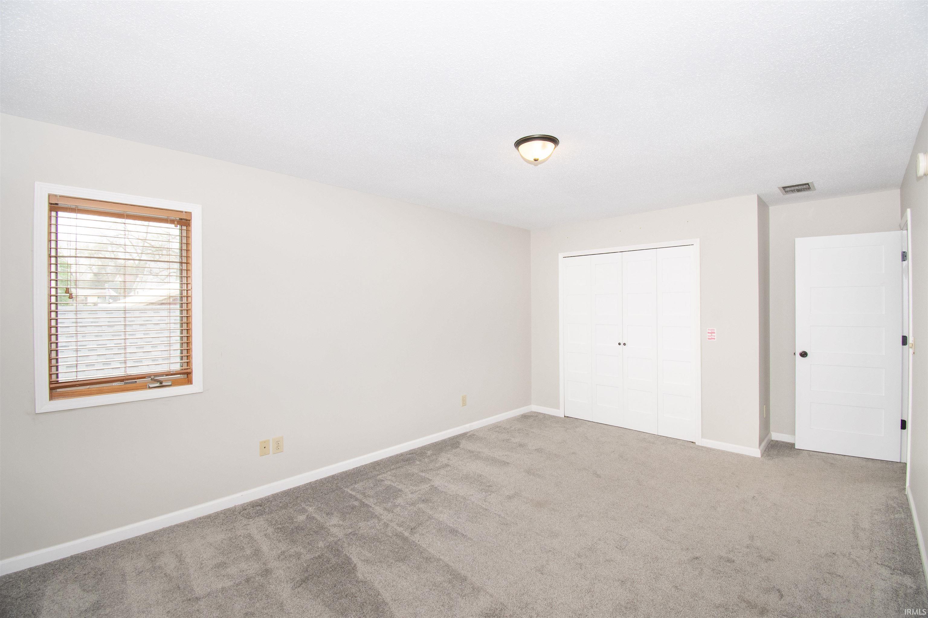 Carpeted room with light gray walls, a window with wood blinds, a flush mount ceiling light, and white bi-fold closet doors