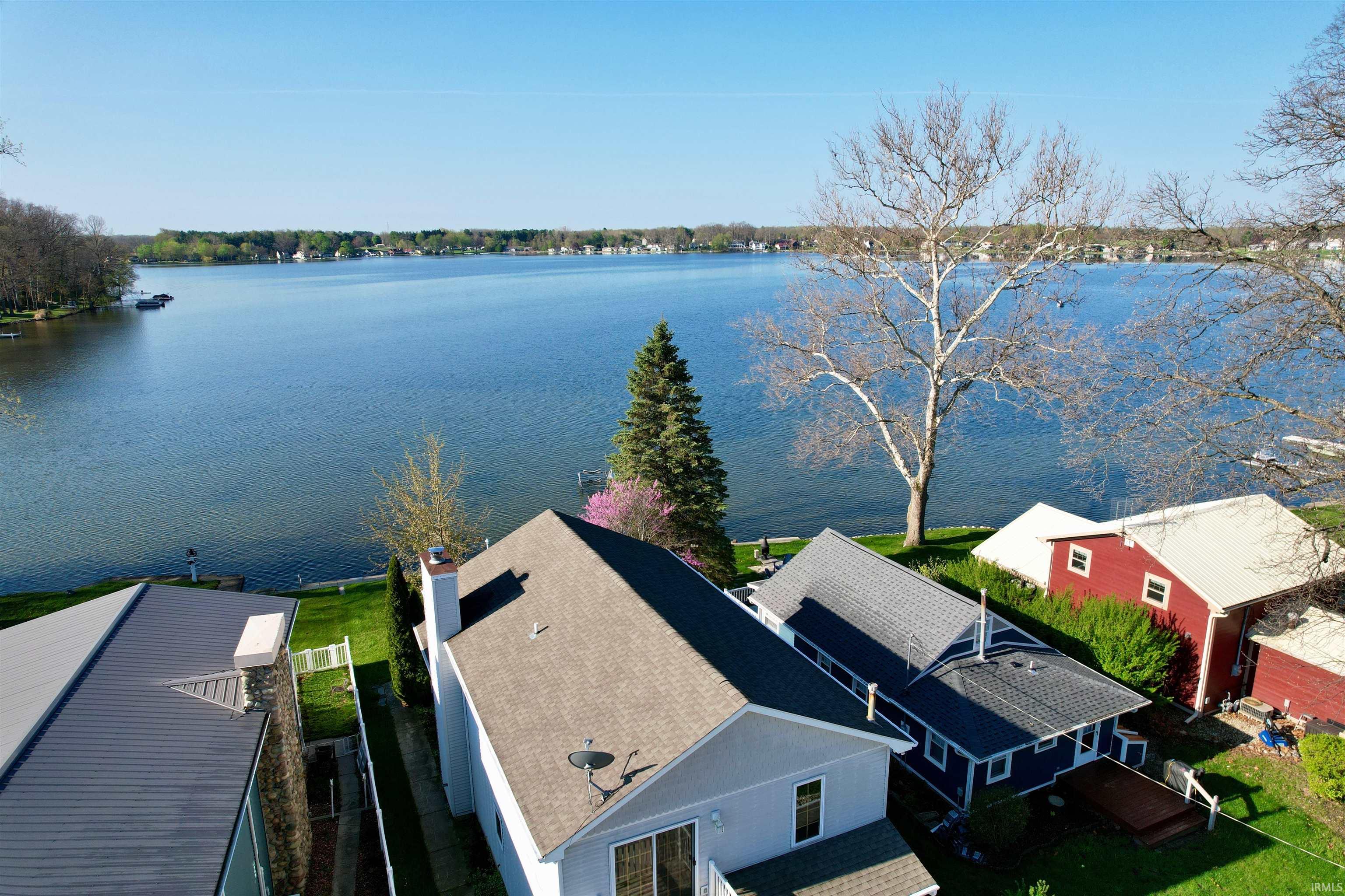 Expansive waterfront property featuring a substantial body of water, green lawn, a large deciduous tree, and a notable evergreen tree