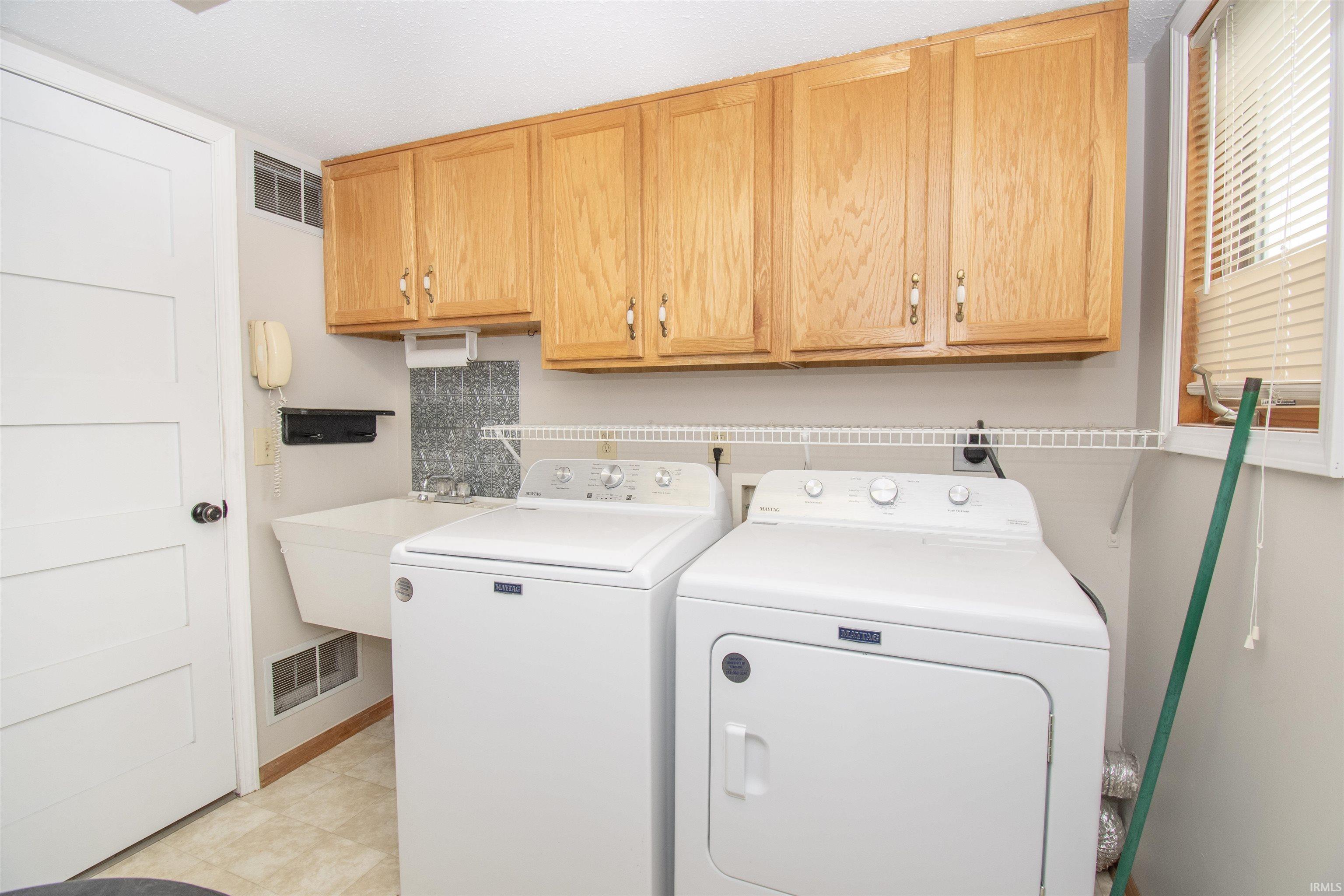 Dedicated laundry area featuring a utility sink, a window with blinds, and wood cabinetry