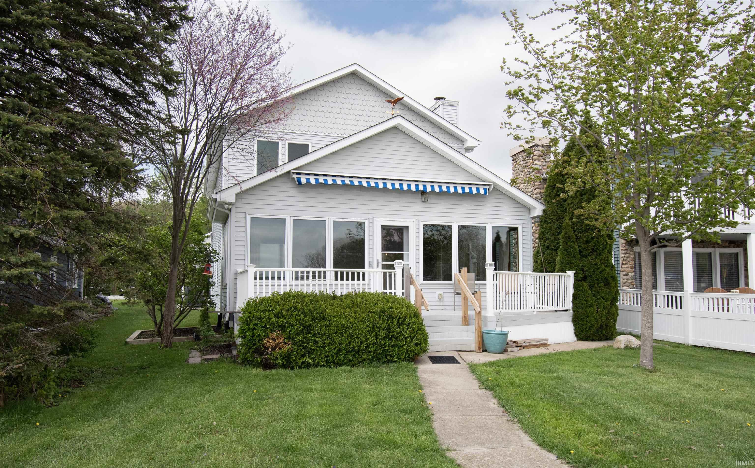 Two-story siding exterior with an awning-covered sunroom, a white railing porch, a front walkway, and a green lawn