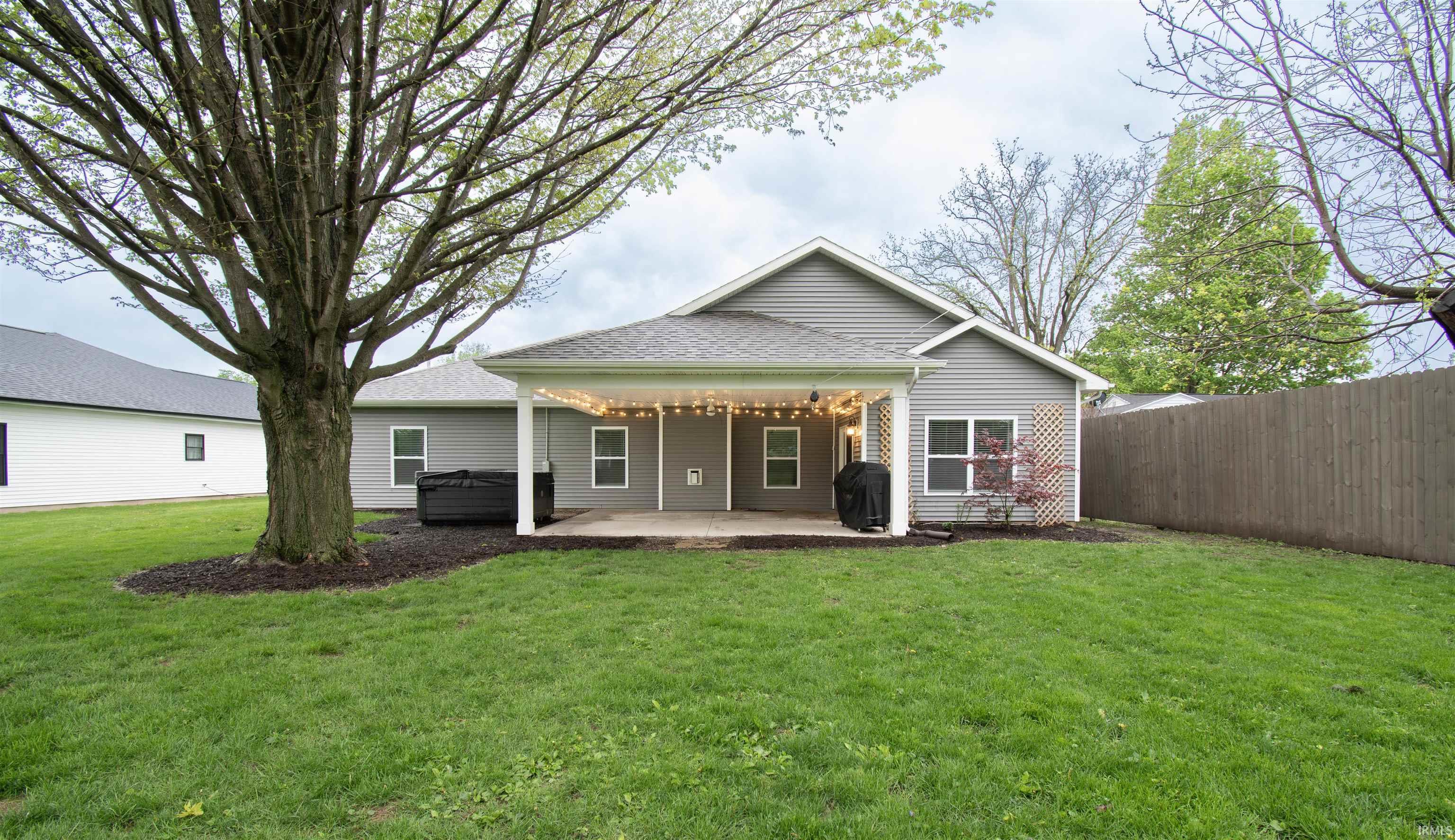 Expansive grassy backyard featuring a covered patio with string lighting, a privacy fence, and mature trees