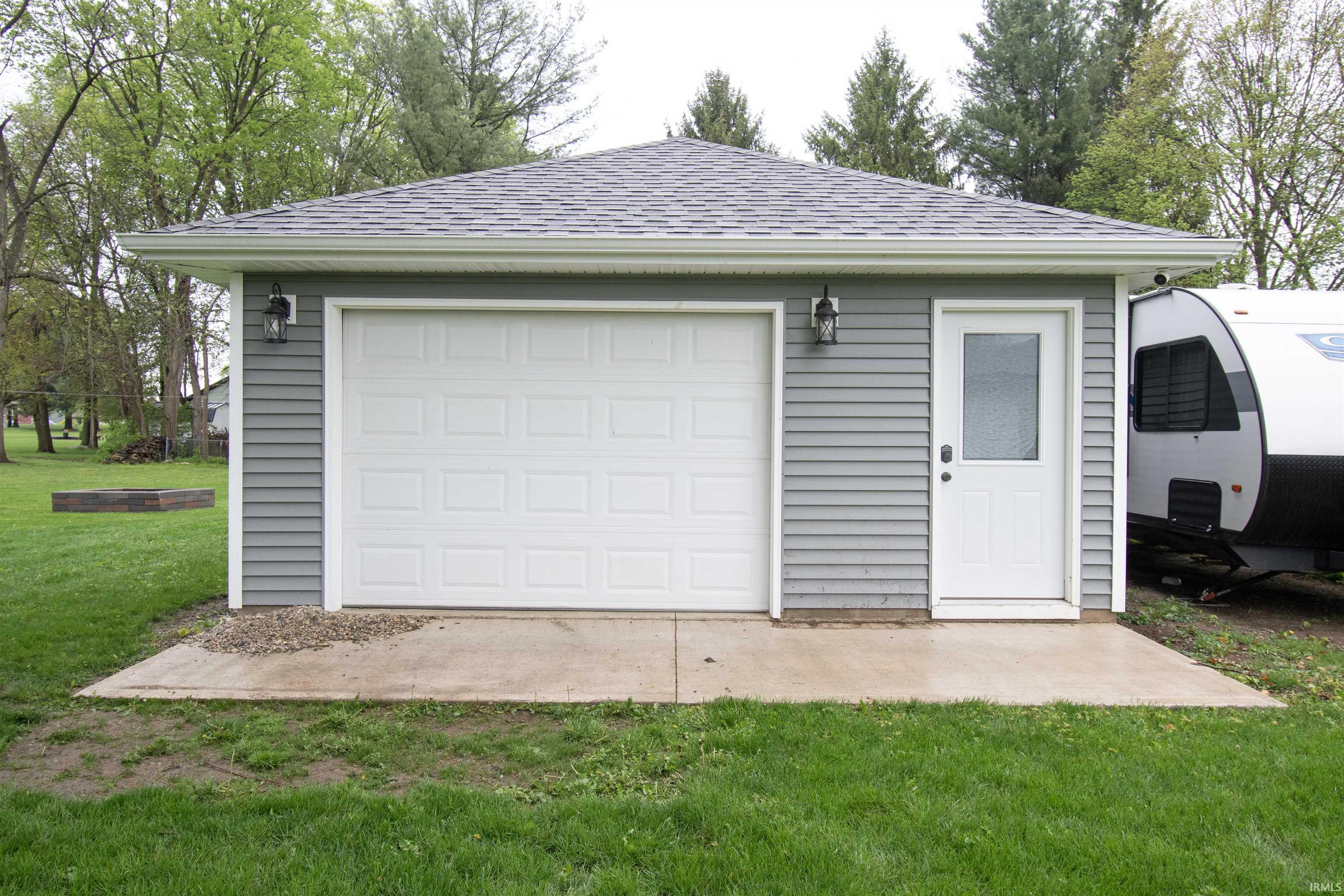 Detached garage with gray horizontal siding, a white panel garage door, and a white entry door with a frosted glass pane