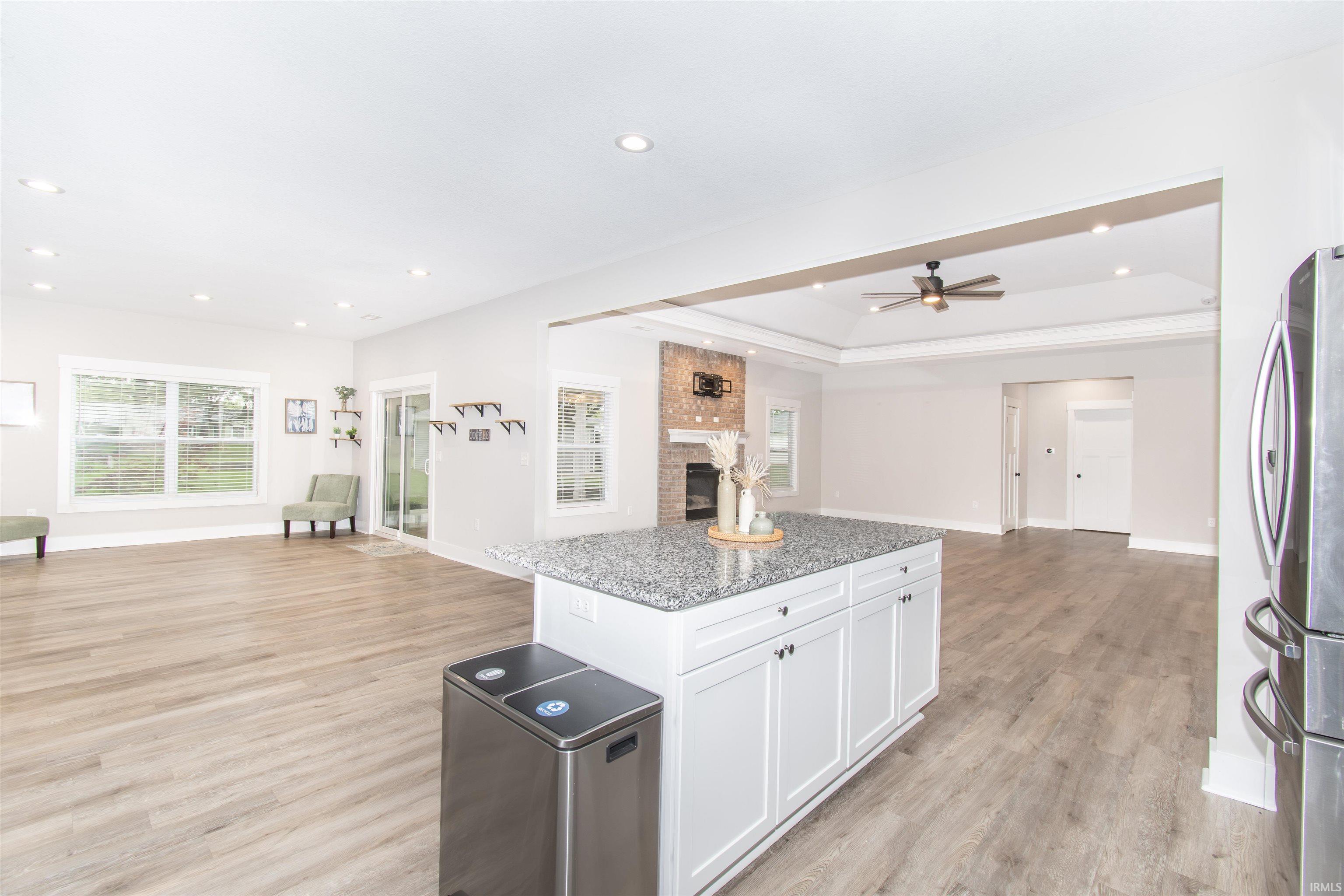 Open-concept living area with wood-finish flooring, recessed lighting, and a white kitchen island featuring a stone countertop and white cabinetry