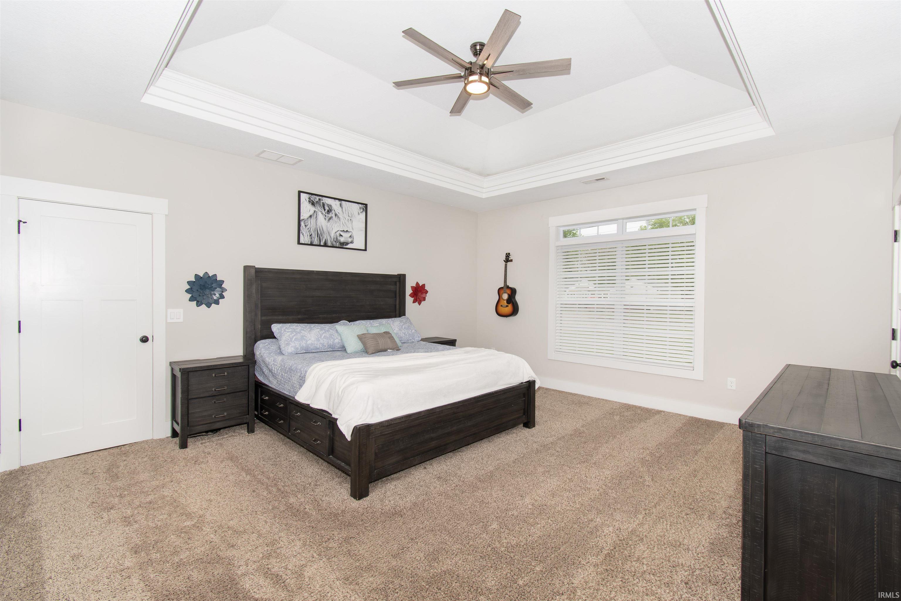 Recessed tray ceiling with crown molding, ceiling fan with integrated lighting, and a double-hung window with blinds