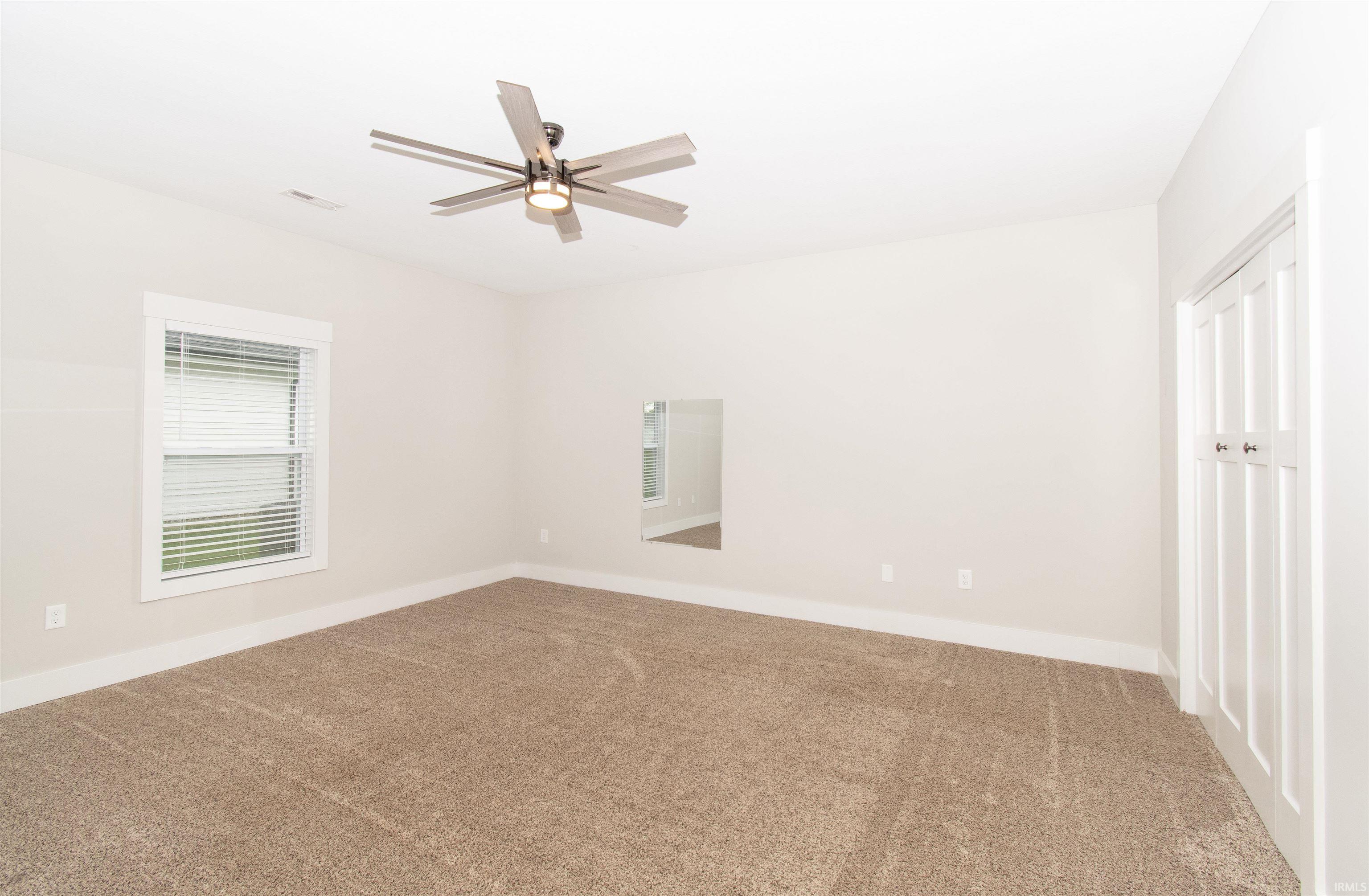 Spacious room featuring neutral carpeting, light-colored walls, and a multi-blade ceiling fan with integrated lighting