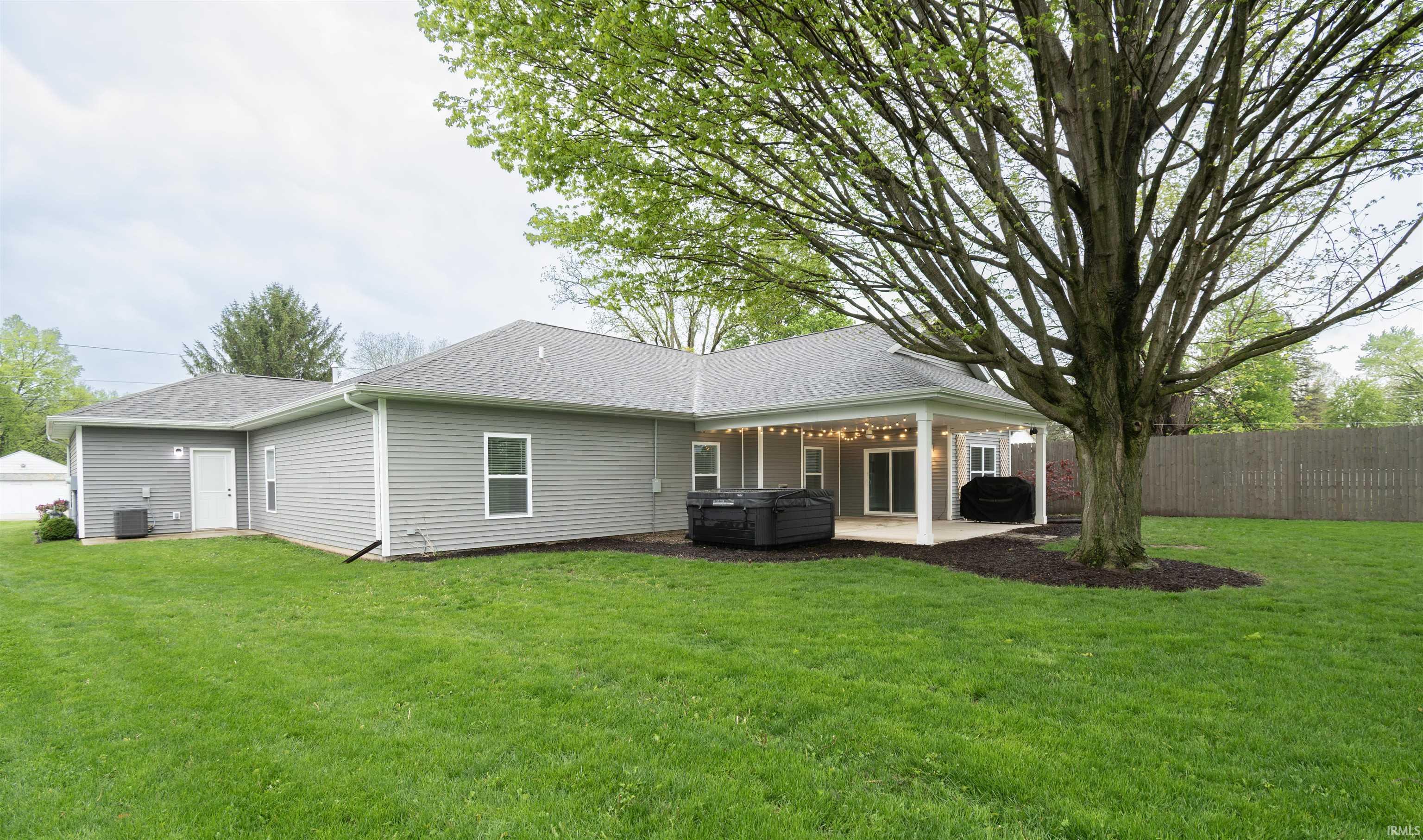 Expansive rear yard featuring a covered patio, mature tree, and privacy fencing