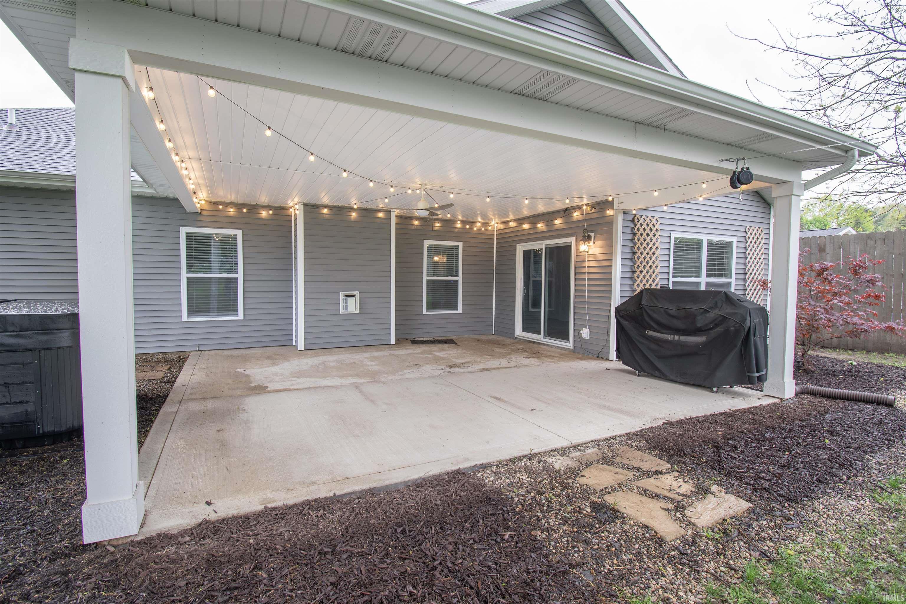 Expansive covered patio featuring a concrete surface, white support columns, and string lighting