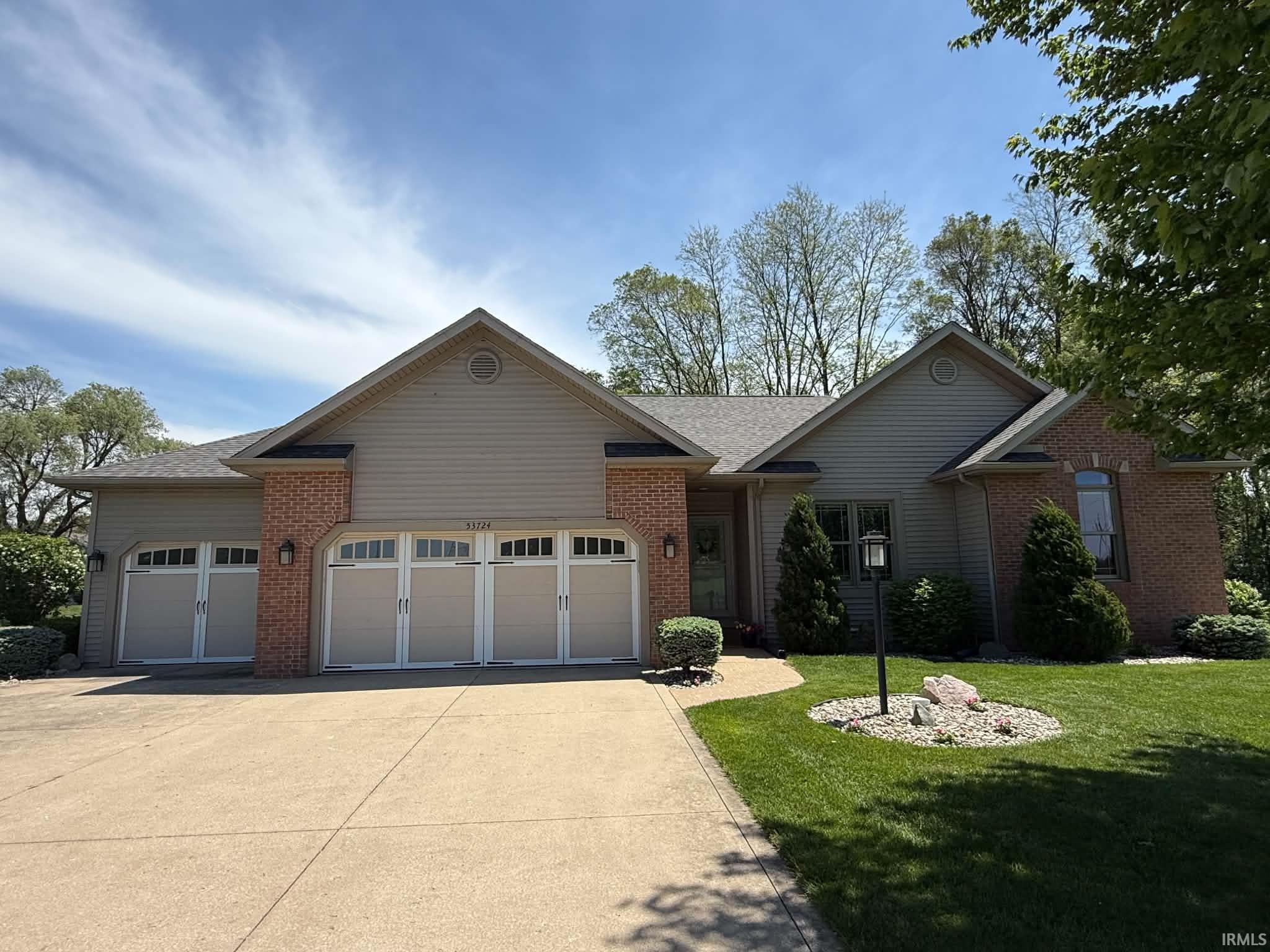 Brick and siding exterior featuring a multi-gabled roofline, three garage doors with decorative window inserts, an arched entryway, and a concrete driveway