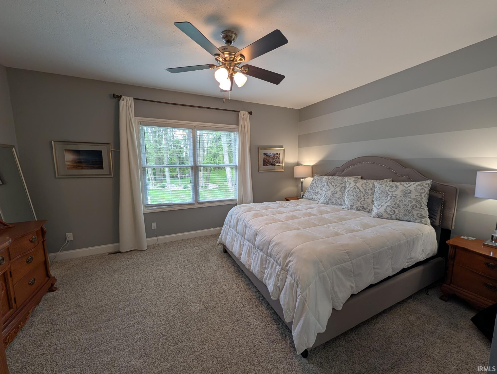 Carpeted room featuring a ceiling fan with light fixture, large window with blinds and curtains, and a striped accent wall