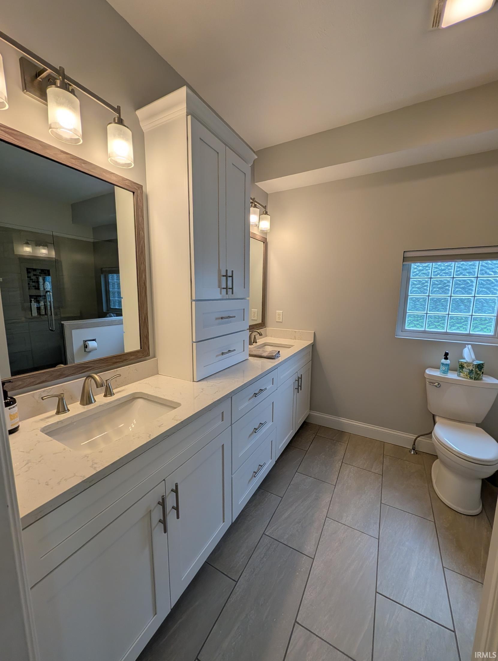 Bathroom featuring a dual vanity with white cabinetry, light-colored countertops, and brushed nickel hardware