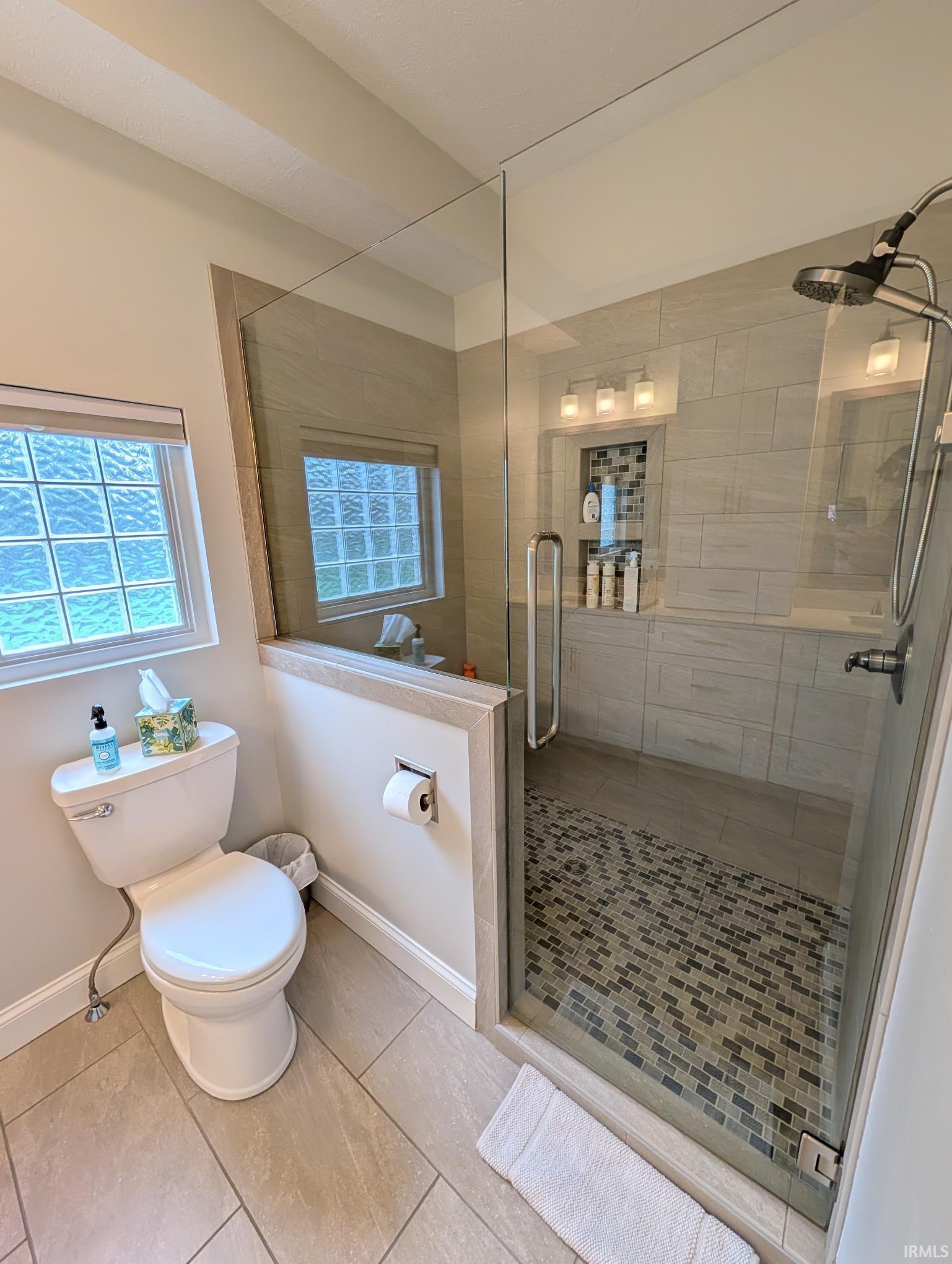 Glass-enclosed shower featuring a mosaic tile floor, built-in shelving, and a wall-mounted showerhead