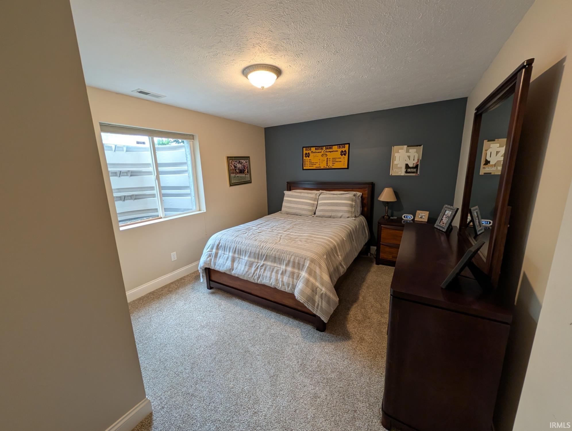 Comfortable room featuring a neutral carpet, a window with a white window well, and a contrasting accent wall