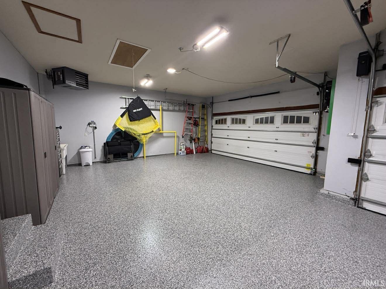 Spacious garage featuring a durable epoxy floor, integrated overhead lighting, and two large garage doors