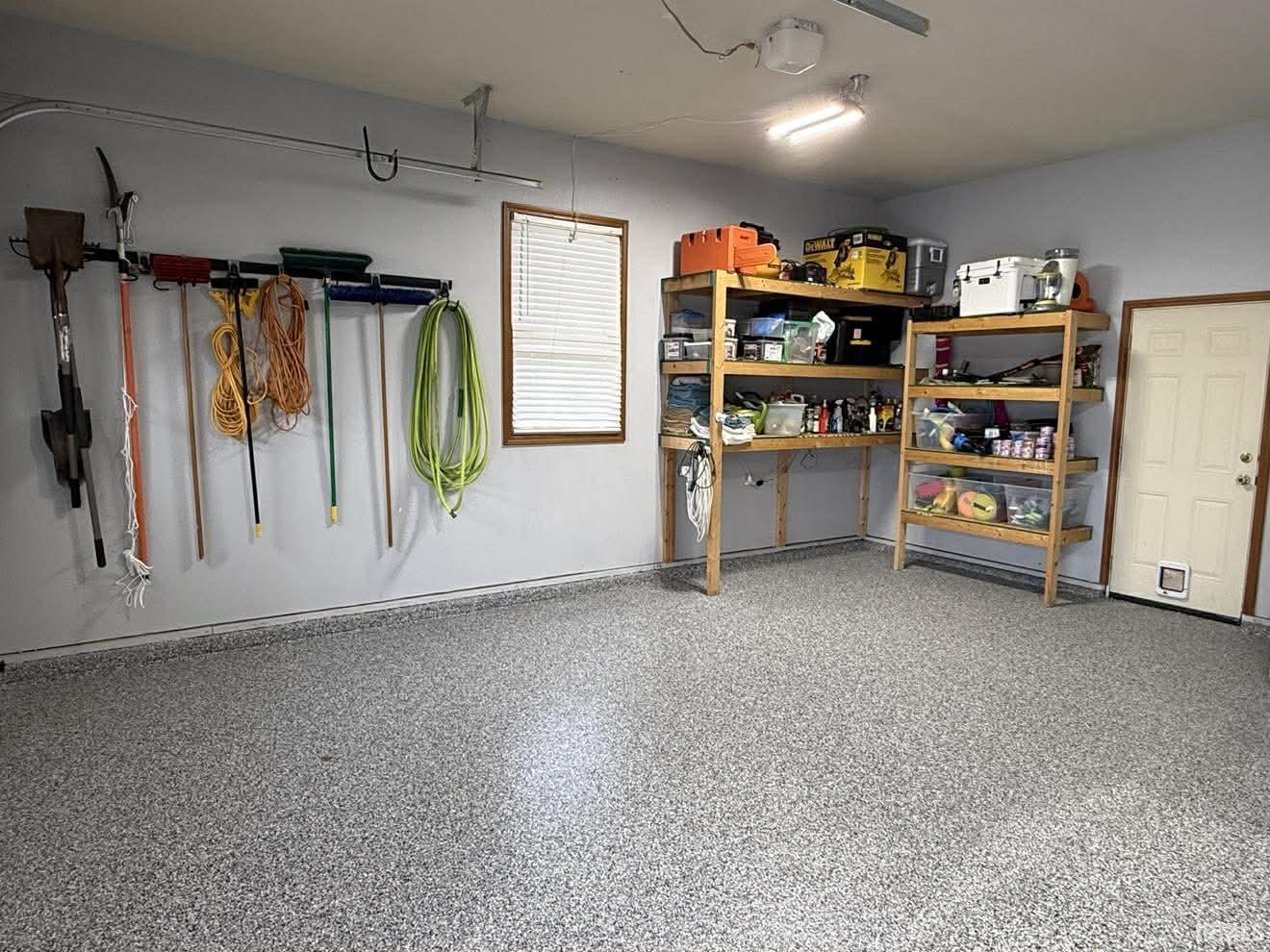 Garage with speckled epoxy flooring, painted walls, built-in shelving, a window with blinds, and a side door