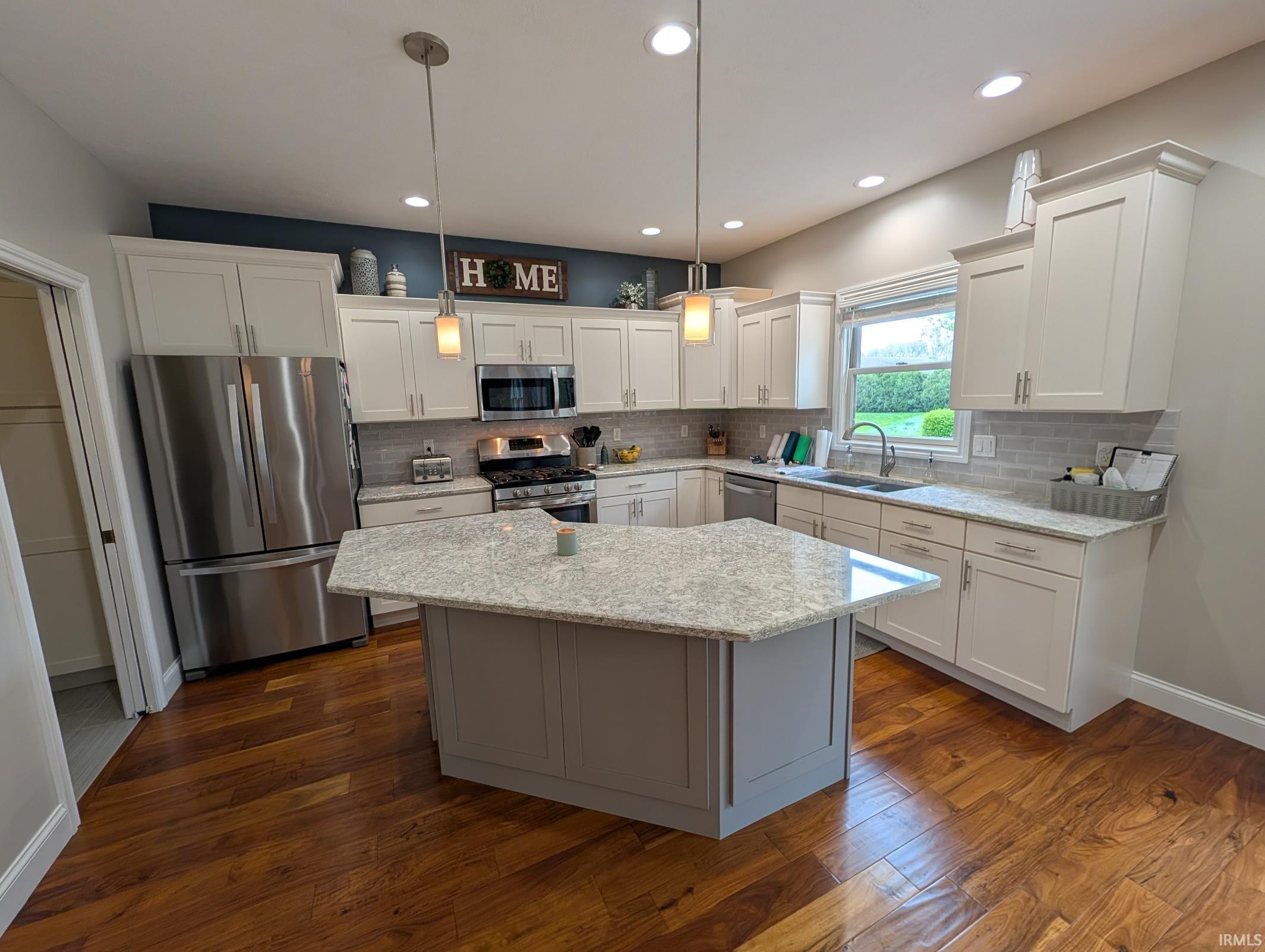 Kitchen featuring a central island with a light-toned countertop, wood-finish flooring, white cabinetry, recessed lighting, and stainless steel appliances