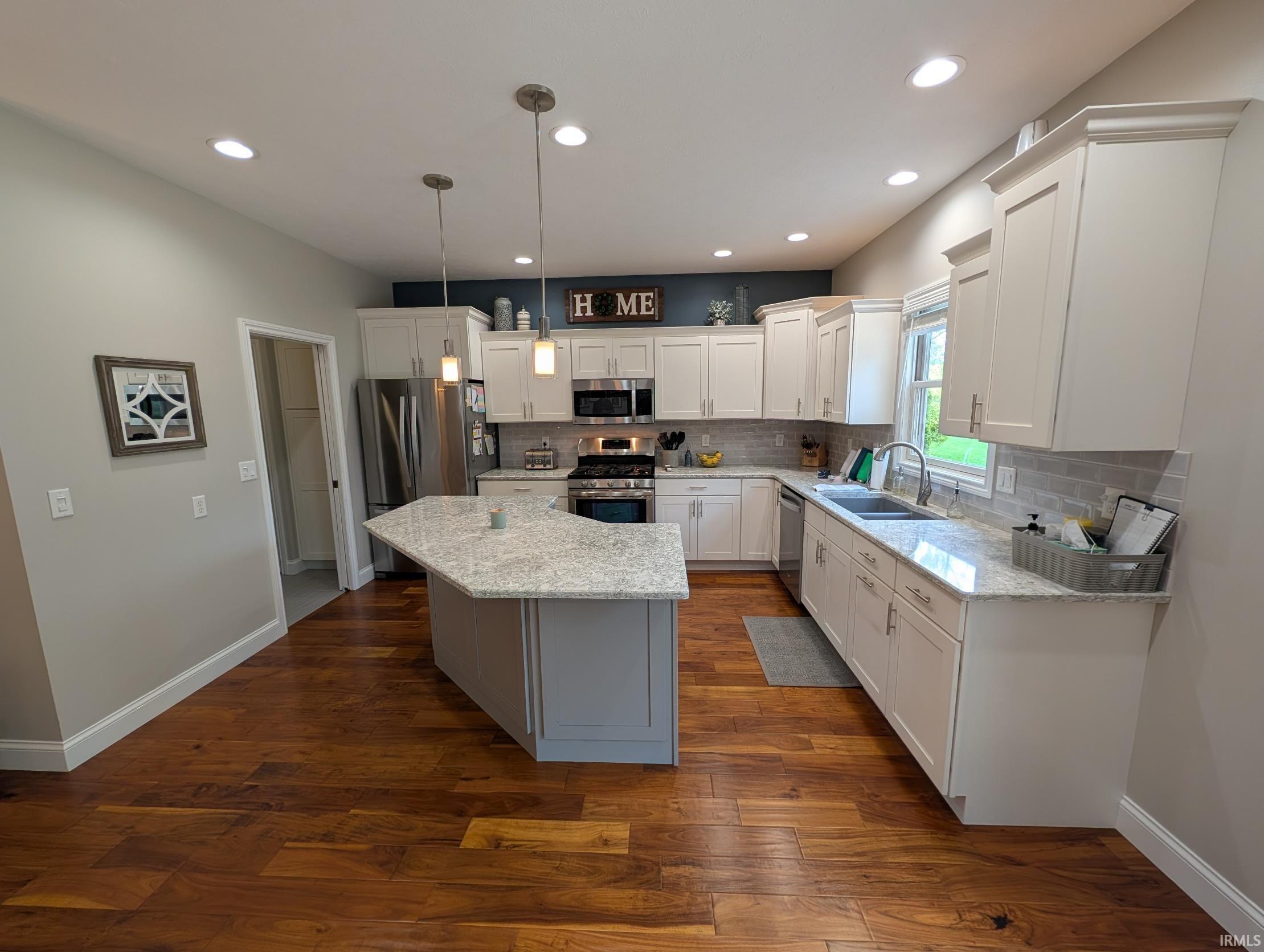 Kitchen featuring a large island with a stone countertop, white shaker cabinetry, stainless steel appliances, and wood-finish flooring