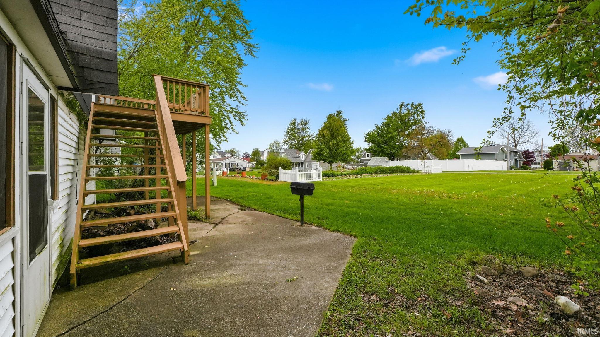 Expansive green yard with a concrete patio and a multi-level wooden deck structure