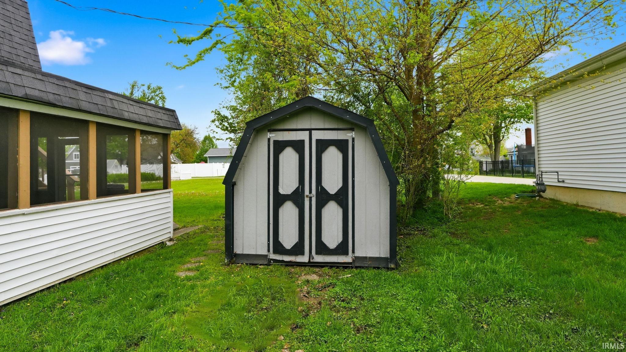 Gable-roofed storage shed with white siding and black trim details, situated on a grass lawn