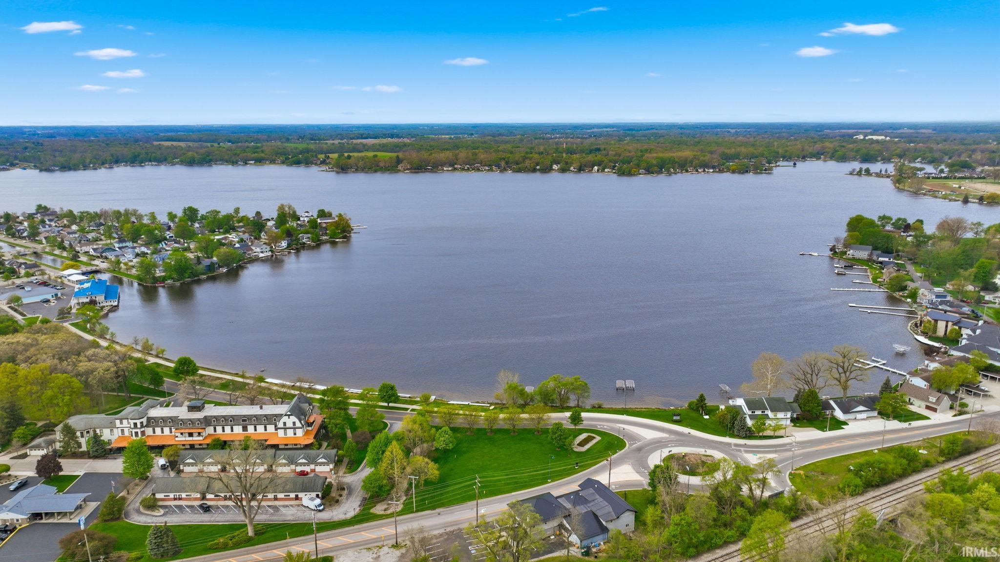 Expansive lakefront property featuring a broad body of water, surrounding residential properties, various docks, and mature perimeter trees