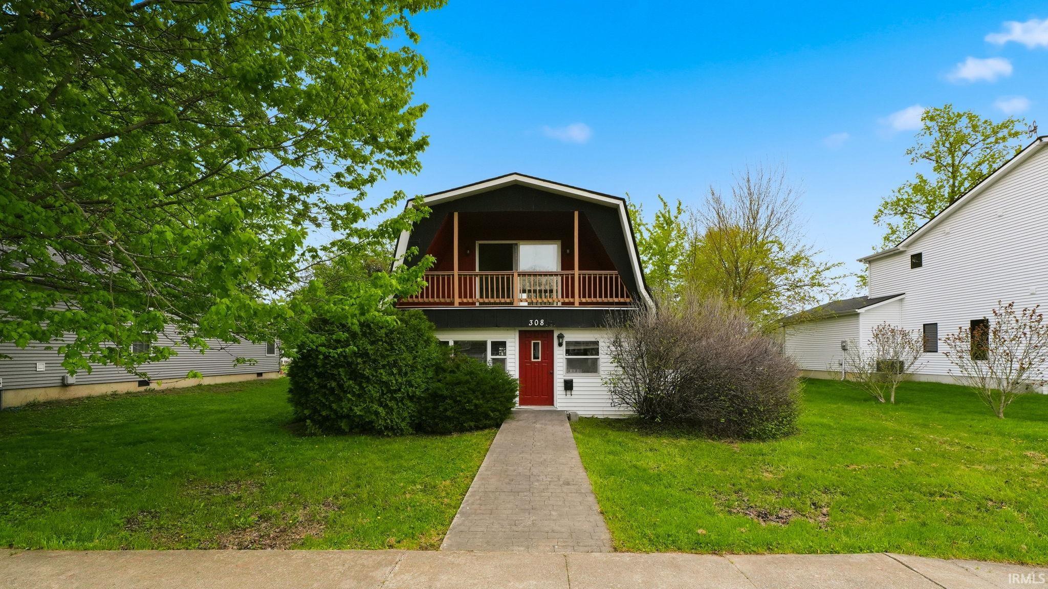 Gabled facade home featuring a red entry door, second-story balcony with wood railing, and white siding