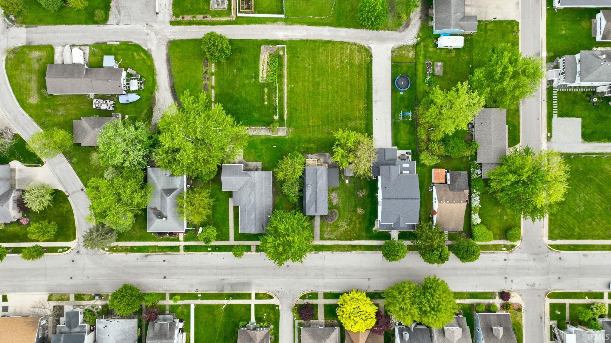 Aerial overview of a residential area featuring multiple detached homes, mature trees, paved streets, and sidewalks