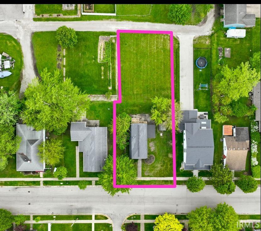 Expansive grassy lot with mature trees, bordered by paved roads