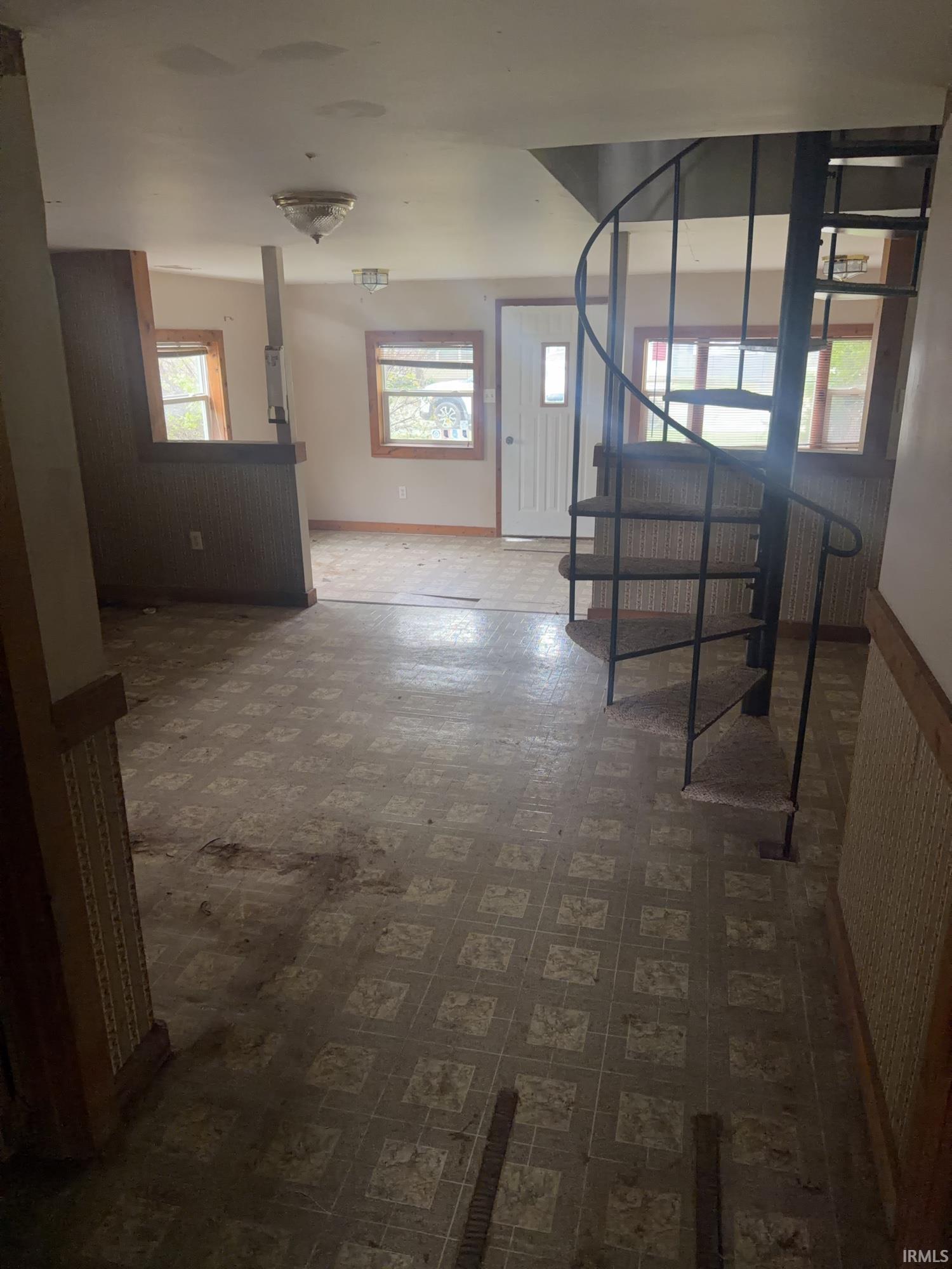 Interior space featuring a spiral staircase, multiple windows with wood trim, a paneled partition wall, a ceiling-mounted light fixture, and patterned flooring