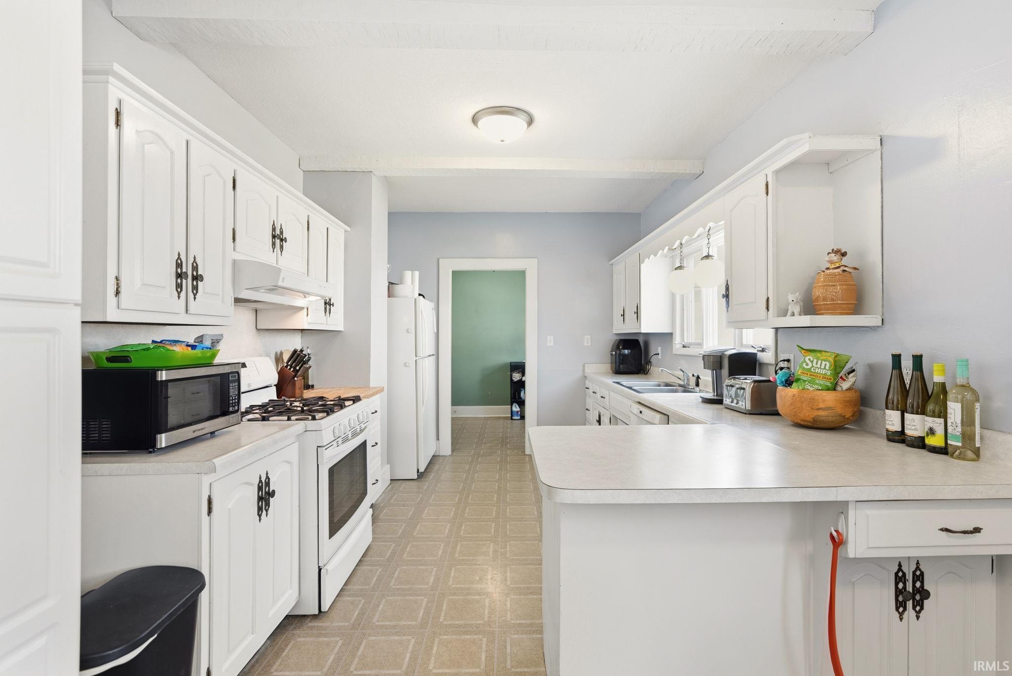 Kitchen with light flooring, white appliances, white cabinets, a peninsula, and light countertops