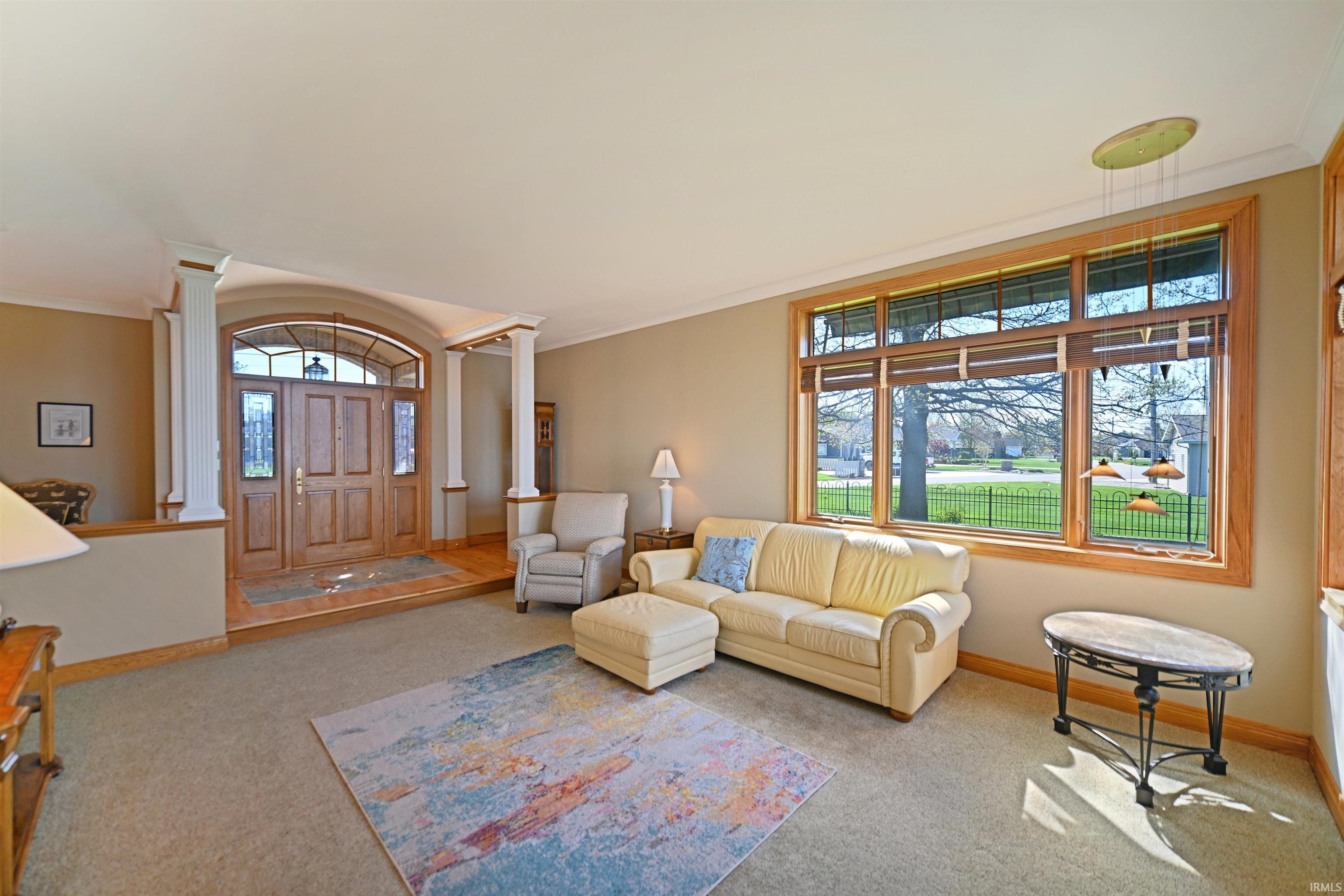 Inviting living area featuring a large window with wood trim, wall-to-wall carpeting, and crown molding