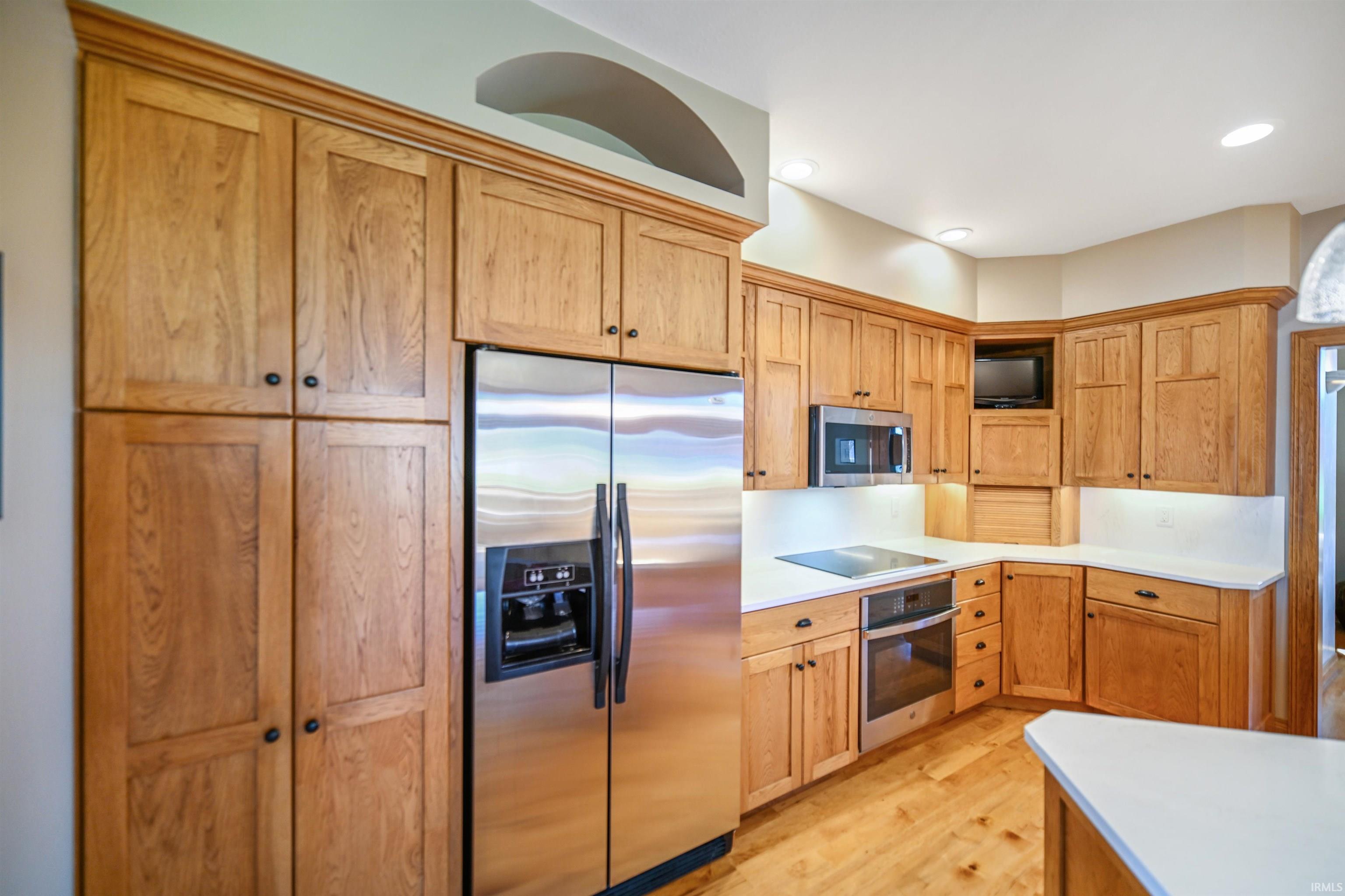 Kitchen featuring wood-finish cabinetry, stainless steel refrigerator, built-in microwave, white countertops, and wood-finish flooring