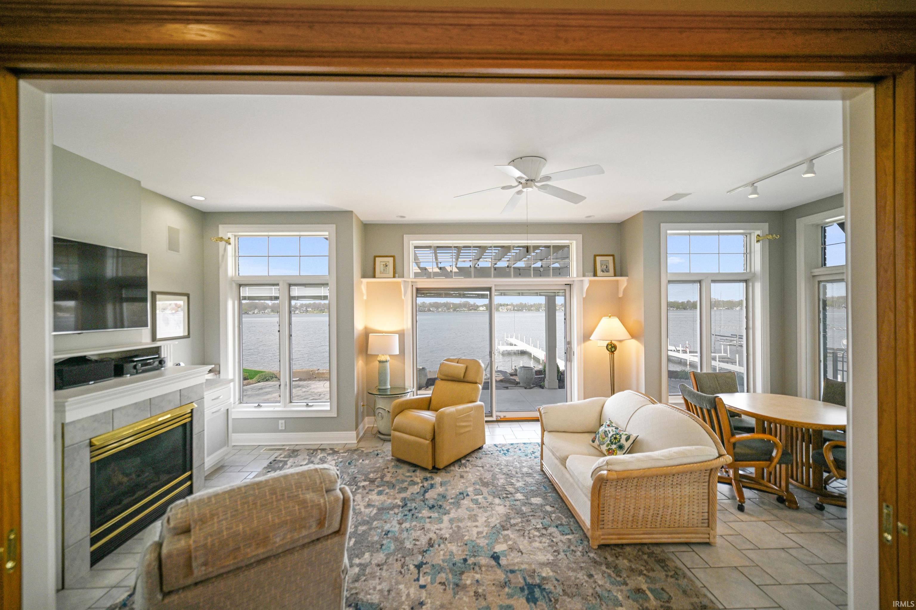 Spacious living area featuring expansive water views, a tiled fireplace with a white mantle, an overhead ceiling fan, and sliding glass doors opening to an outdoor area