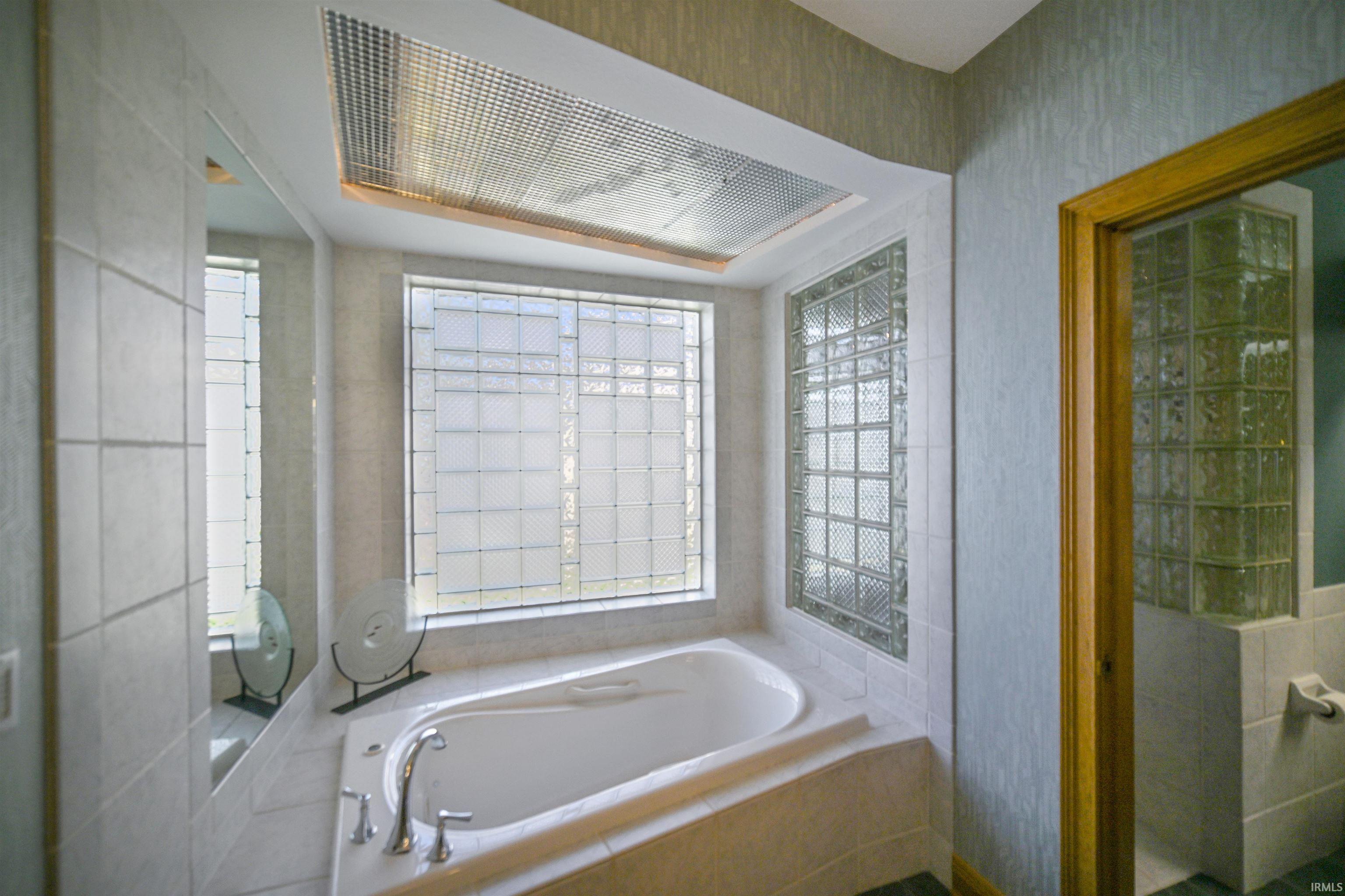 Soaking tub with deck-mounted chrome fixtures, surrounded by tile walls and a large privacy window
