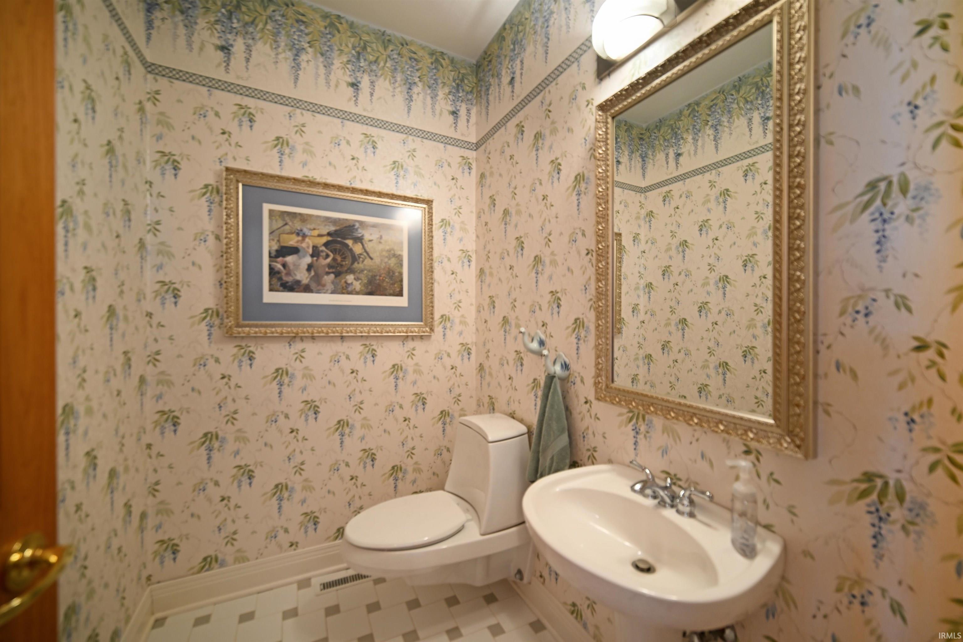 Pedestal sink with chrome fixtures, white toilet, and a decorative gold-framed mirror