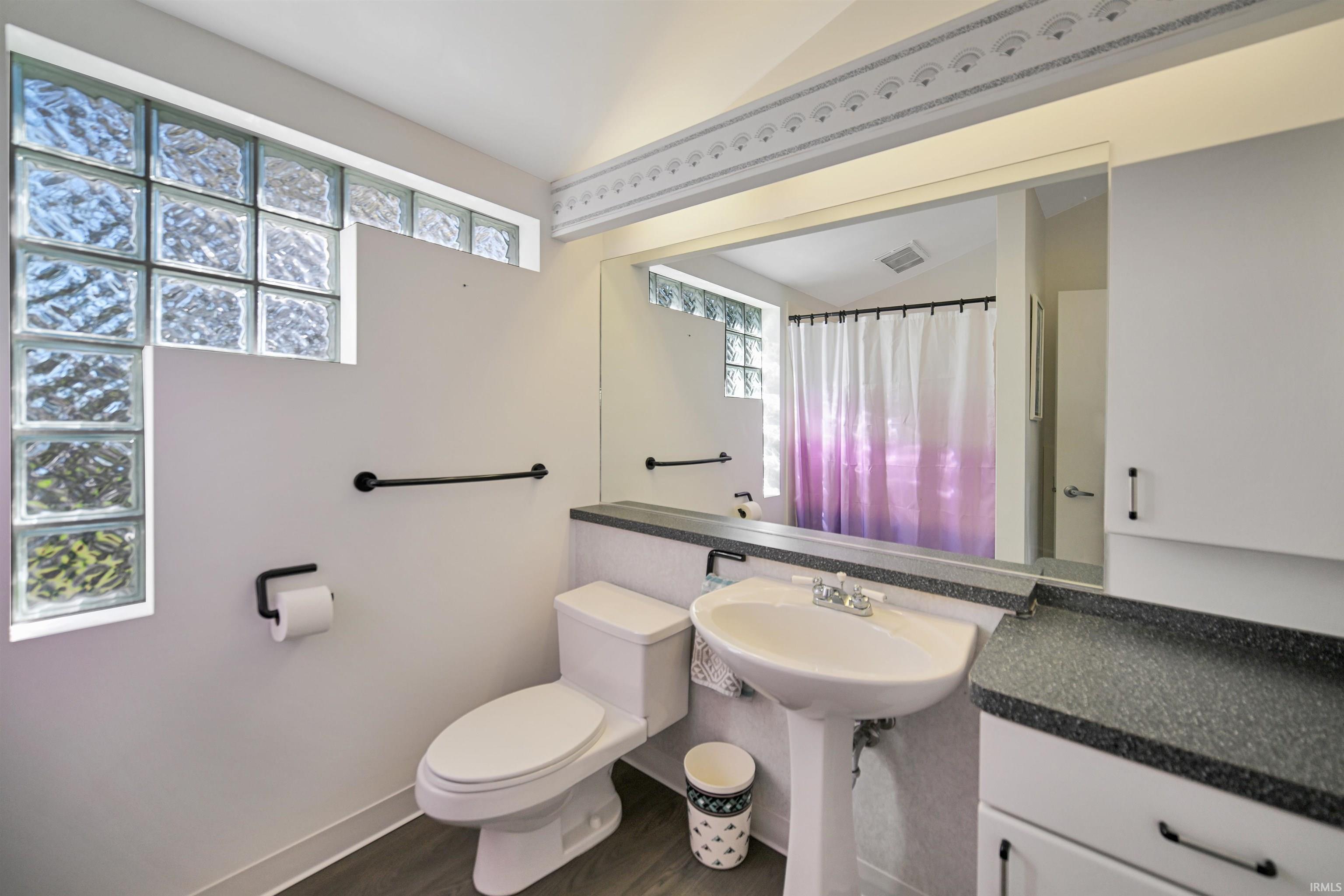 Bathroom featuring a pedestal sink, a toilet, glass block window, and a built-in mirror