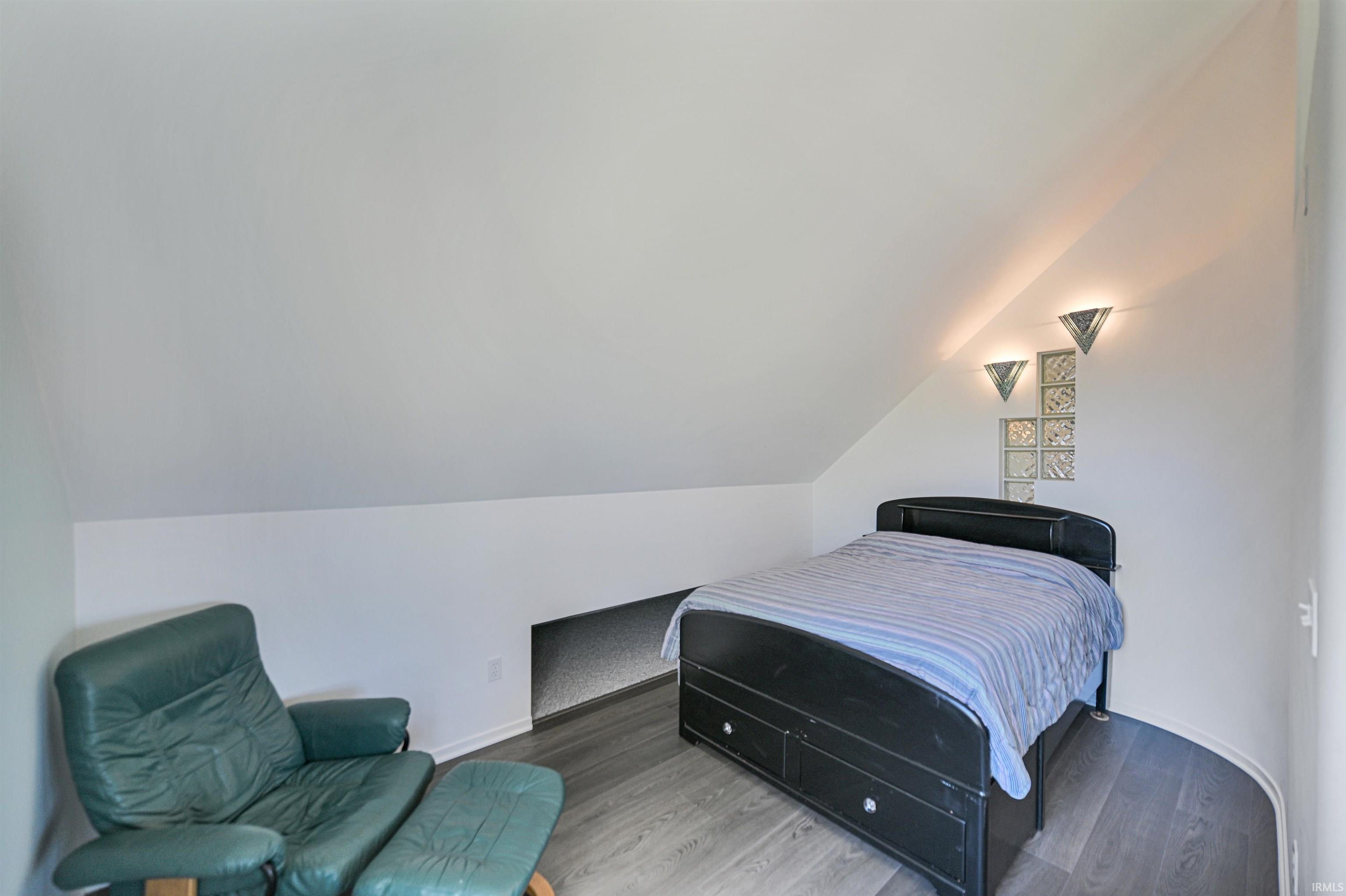 Attic bedroom featuring sloped ceilings, wood-finish flooring, recessed wall niche, and decorative wall sconces with glass block accents