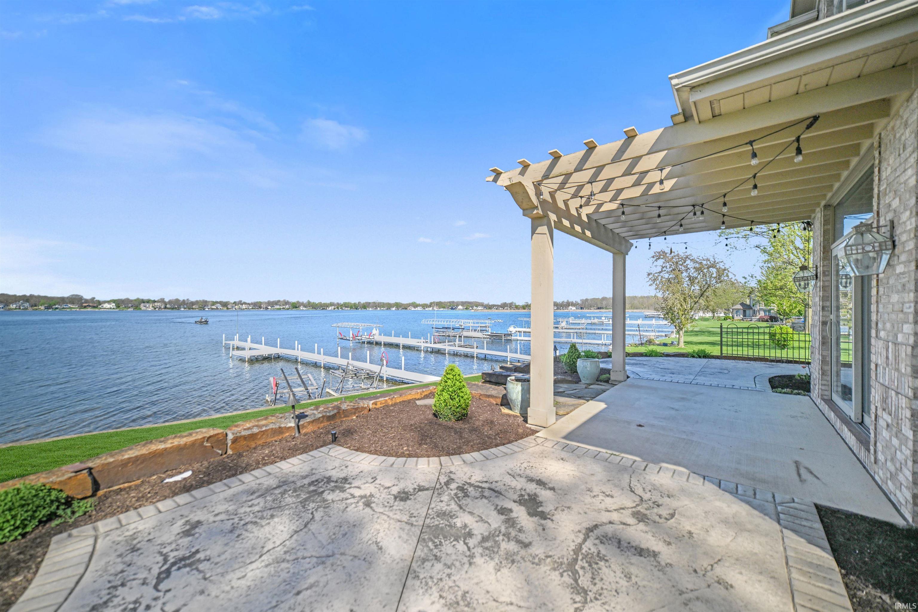 Waterfront property featuring multiple boat docks, a spacious stamped concrete patio, an attached pergola, and a brick exterior with large glass doors