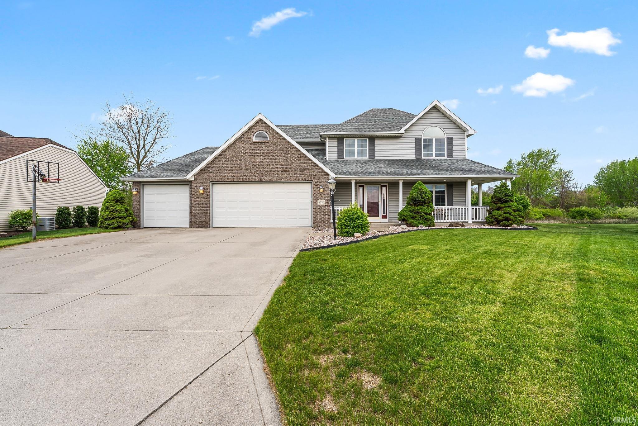 Two-story residence featuring a brick and siding exterior, a welcoming covered front porch with white railings, and a three-car garage