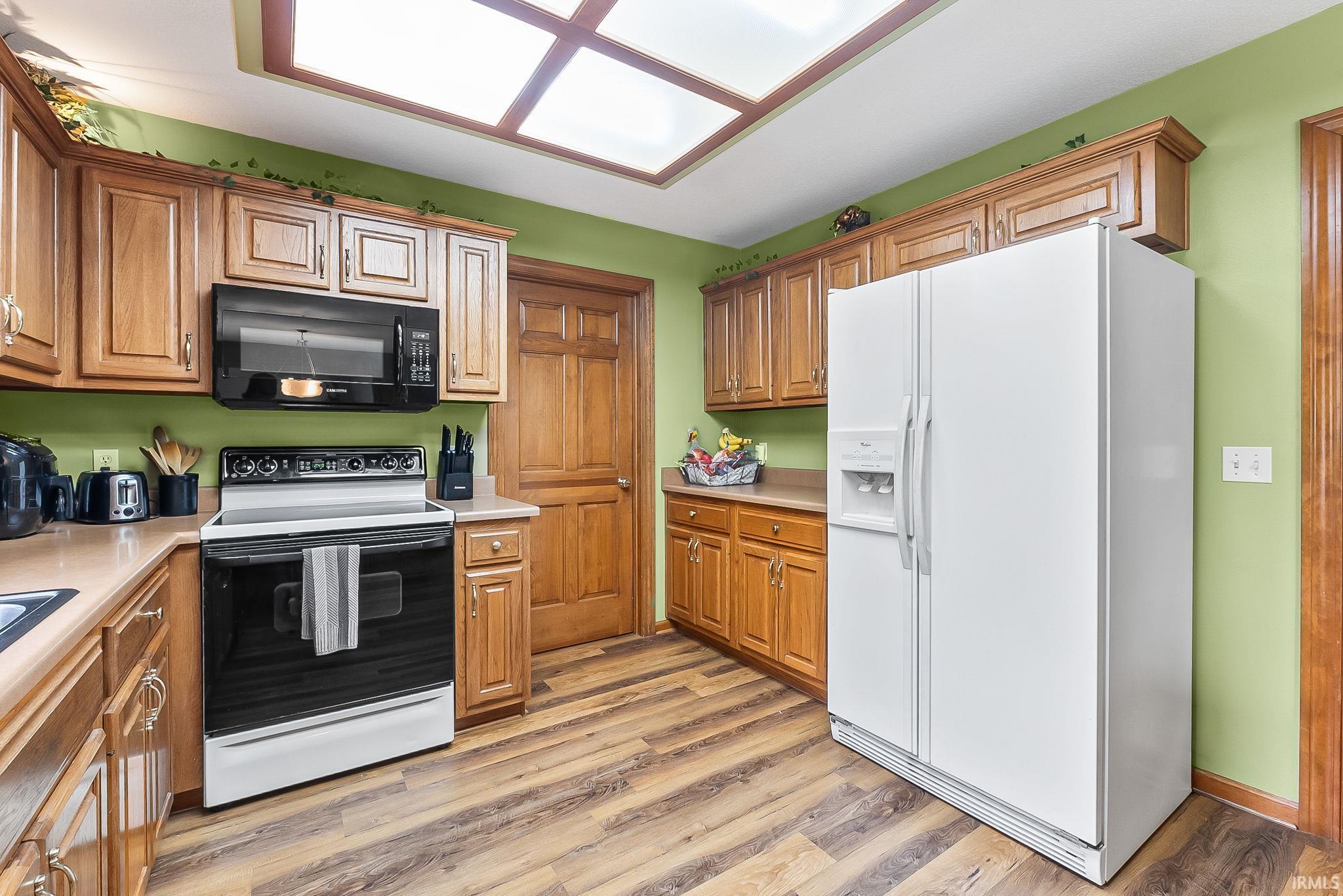 Kitchen featuring wood-finish flooring, wood cabinetry with upper and lower storage, a built-in black microwave, and a white side-by-side refrigerator with dispenser