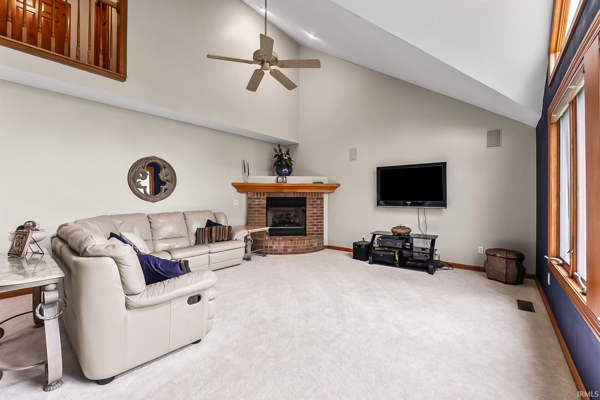 Living area featuring vaulted ceilings, a corner brick fireplace with a wood-finish mantel, and light-toned carpeting