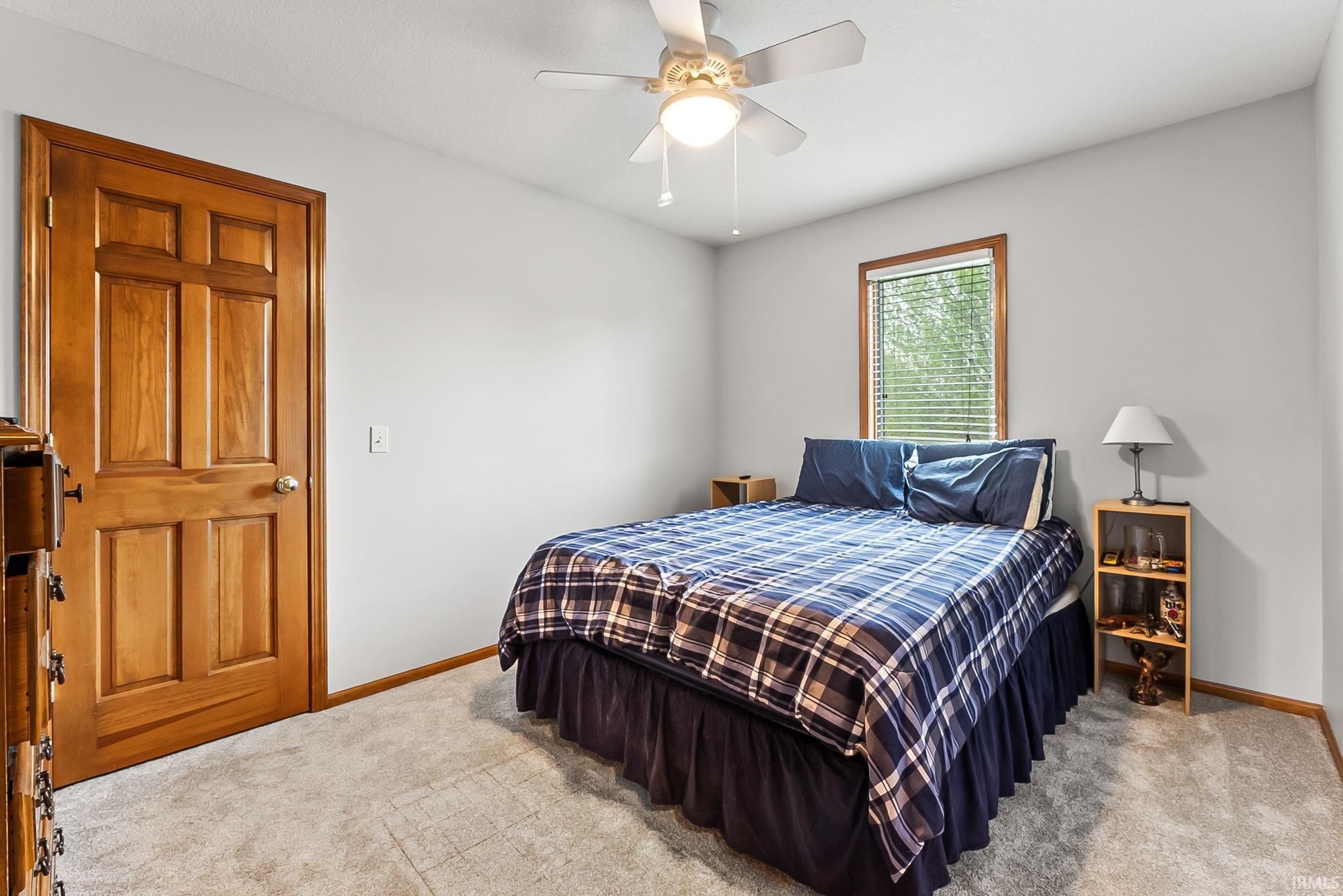 Carpeted room featuring a ceiling fan with integrated lighting, wood-trim window with blinds, and a solid wood paneled door