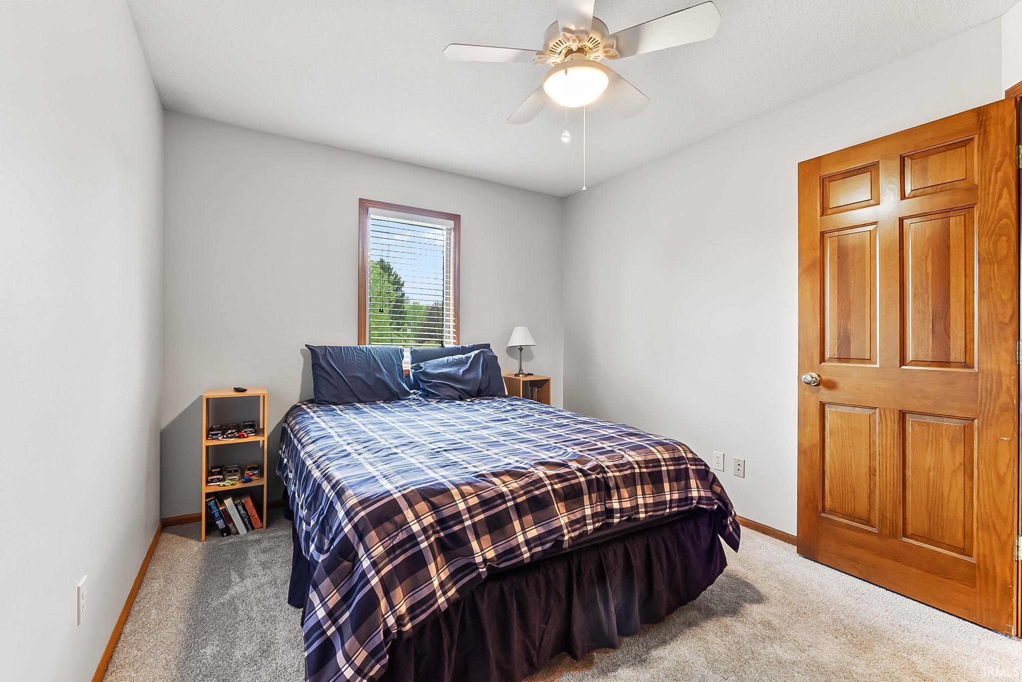 Carpeted room featuring a window with blinds, a wood-finish door, and a ceiling fan with integrated lighting