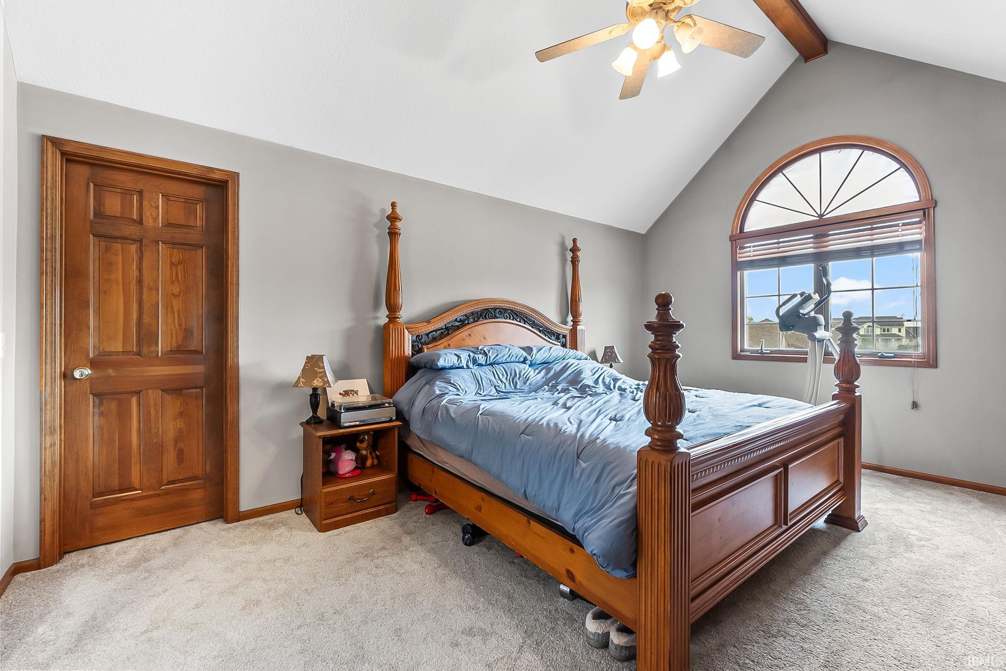 Vaulted ceiling bedroom featuring an arched window, wood-finish window frame, and neutral carpet flooring