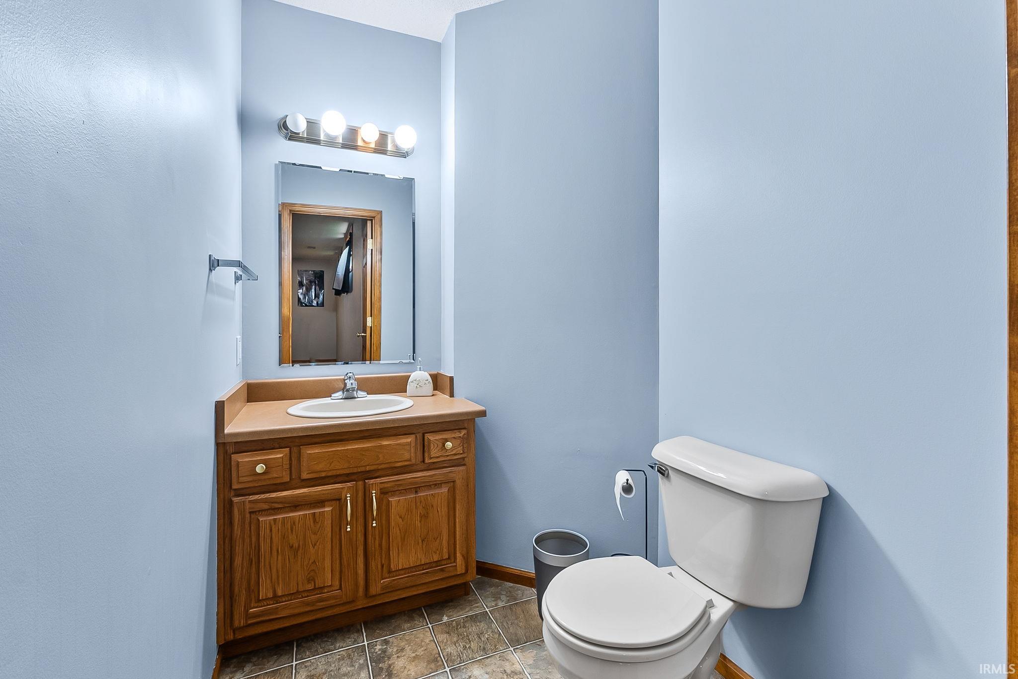 Bathroom featuring a wood-finish vanity with a built-in sink, a wall-mounted mirror, a four-bulb light fixture, and tile flooring