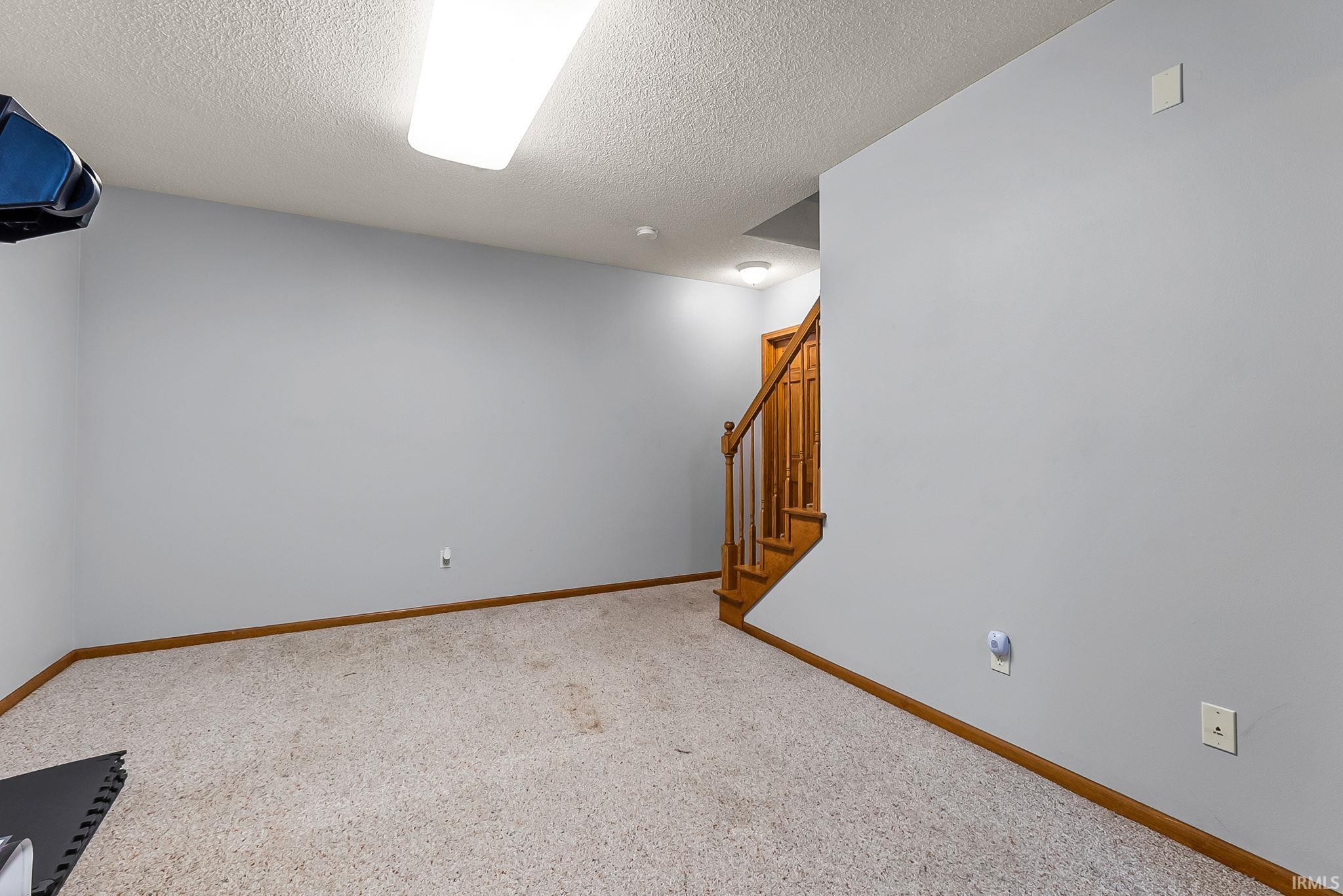 Carpeted room with light gray walls, white baseboards, and a natural wood staircase