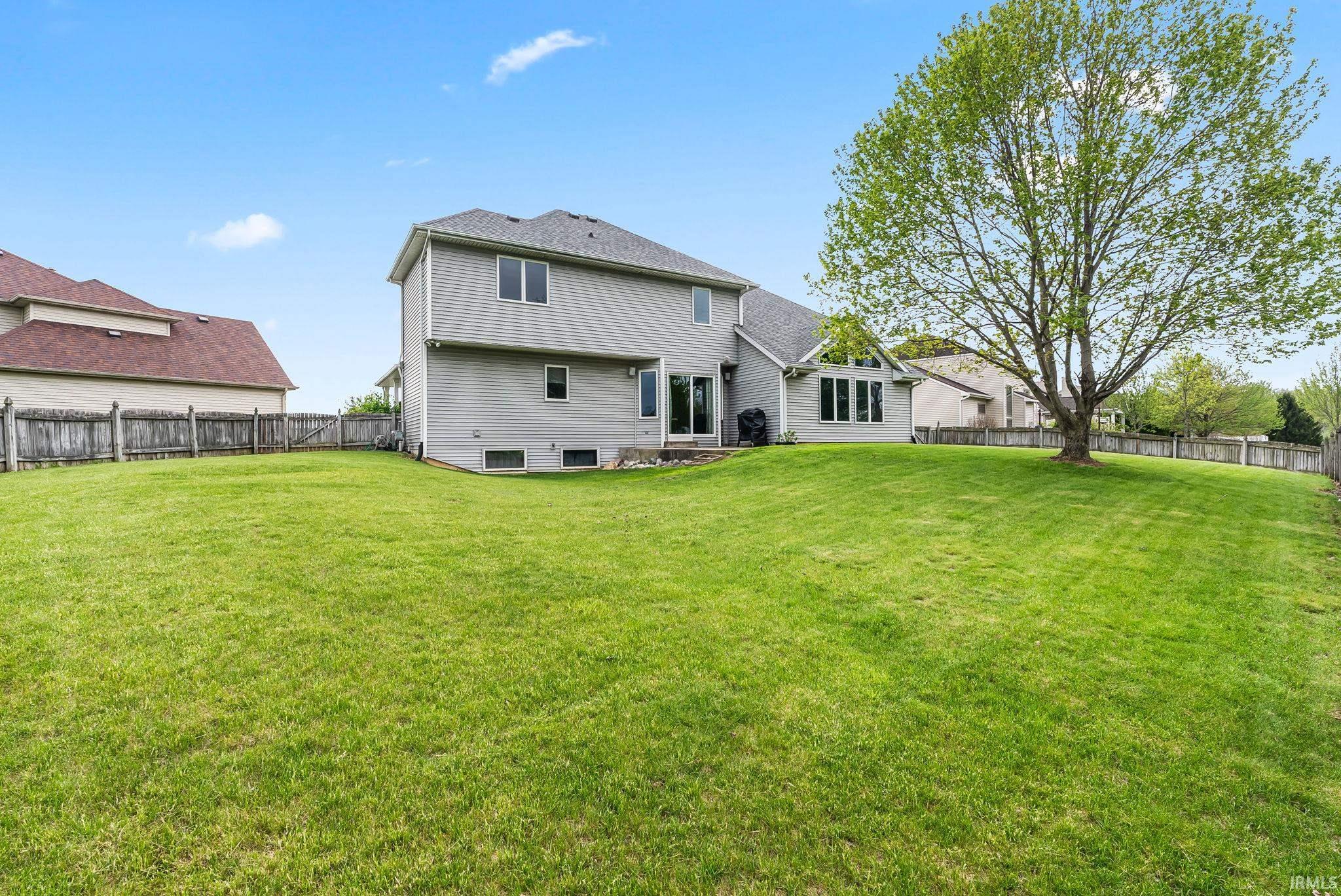 Spacious fenced backyard featuring a large mature tree, expansive green lawn, and walk-out access to the main residence