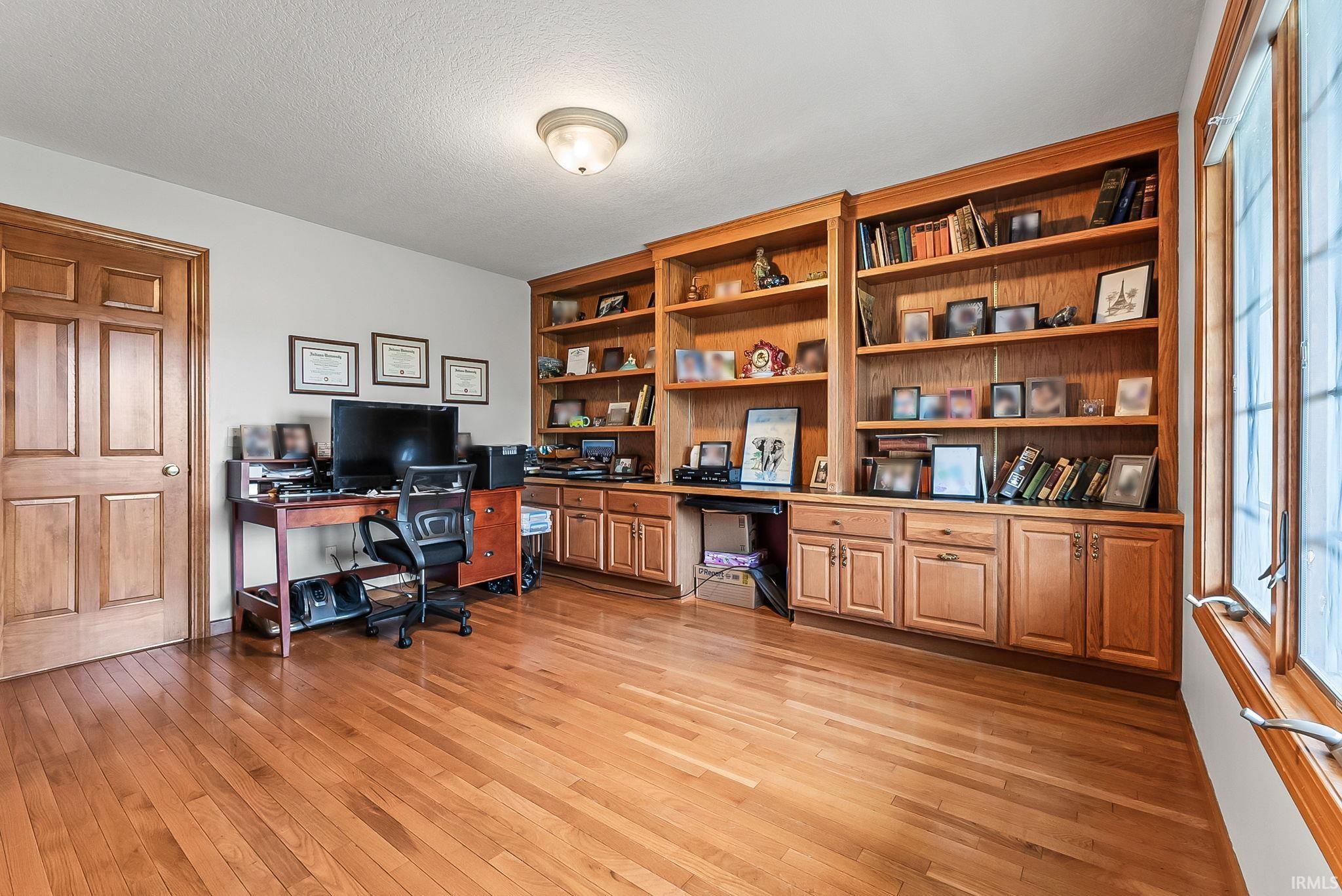Room featuring extensive built-in wooden shelving, integrated cabinetry, wood-finish flooring, a paneled door, and a multi-pane window
