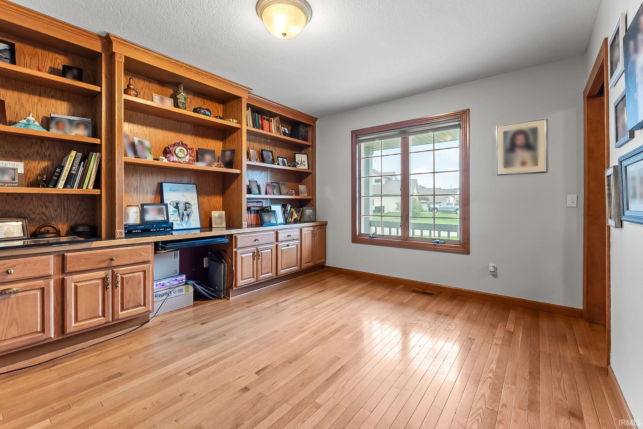 Room featuring extensive built-in cabinetry and shelving, wood-finish flooring, a window with grid patterns, and a flush-mount ceiling light fixture