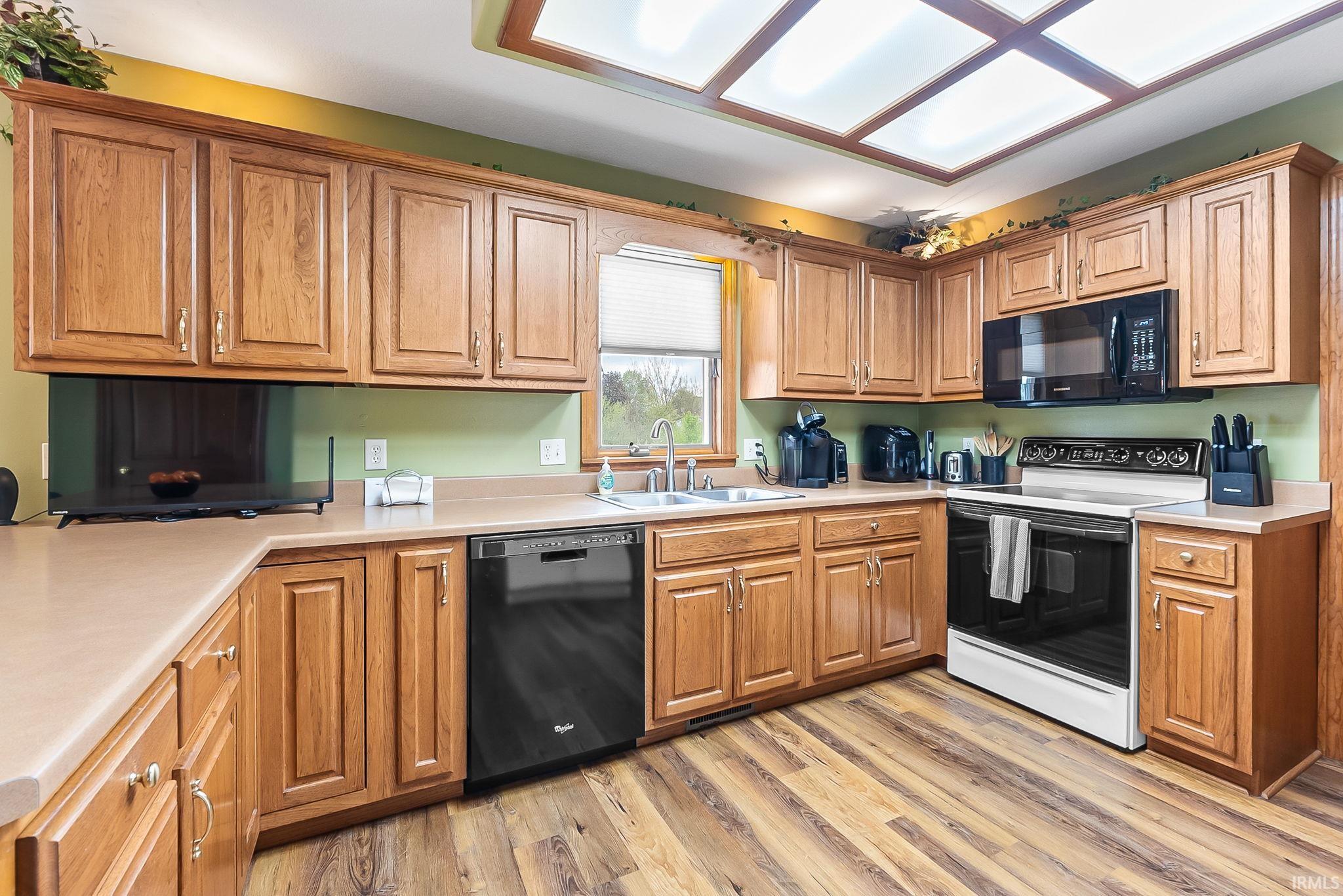 Kitchen featuring wood-finish flooring, recessed lighting, ample cabinetry, a built-in dishwasher, and a window above the sink